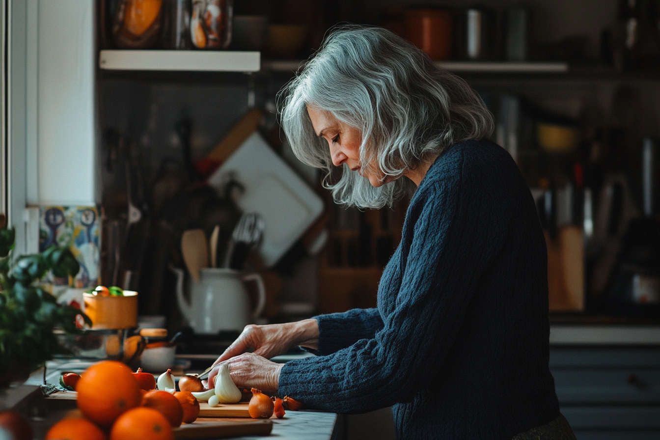 Femme d'une cinquantaine d'années dans la cuisine en train de couper des ingrédients avec concentration | Source : Midjourney