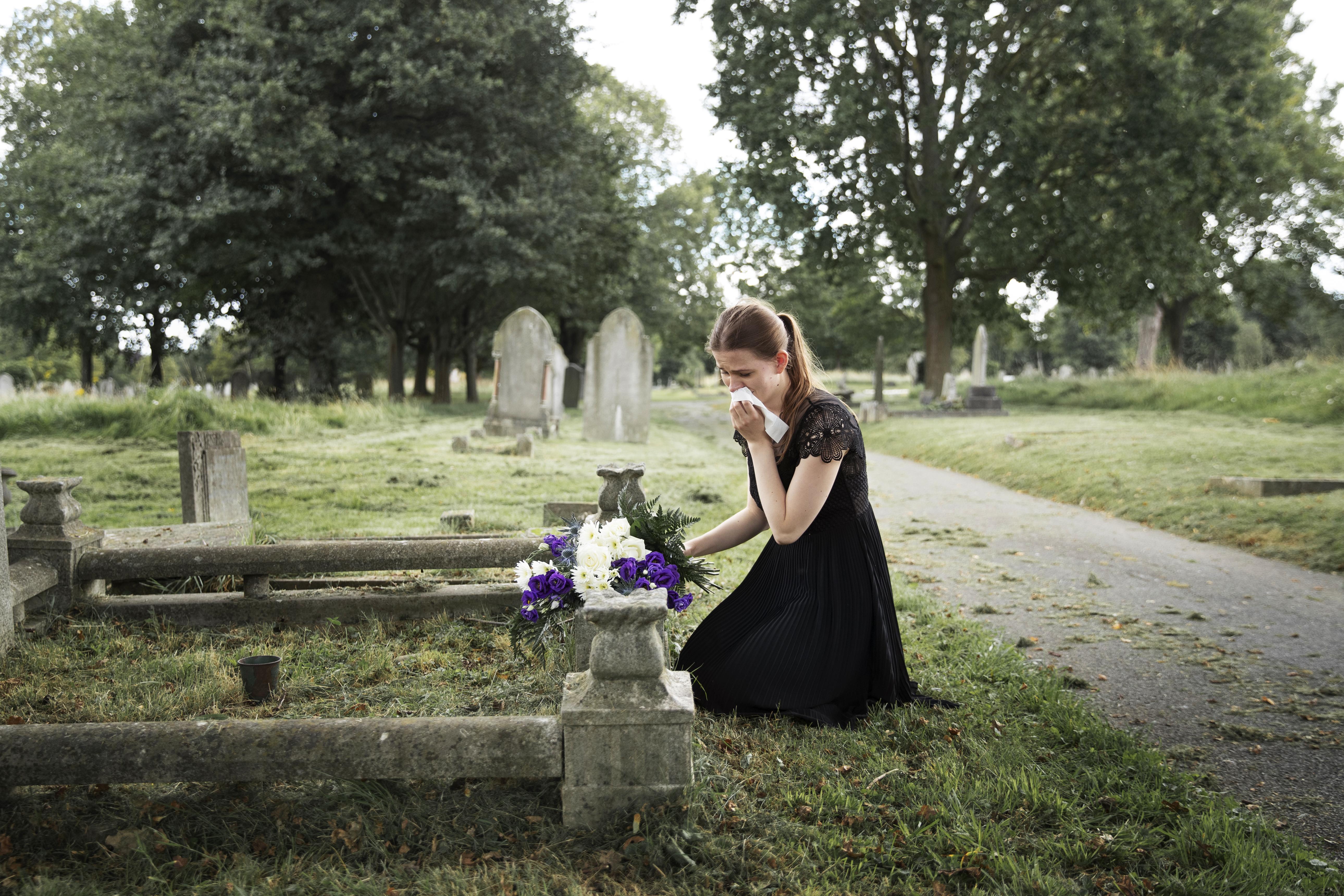 Une jeune femme en deuil près de la tombe d'un être cher | Source : Freepik