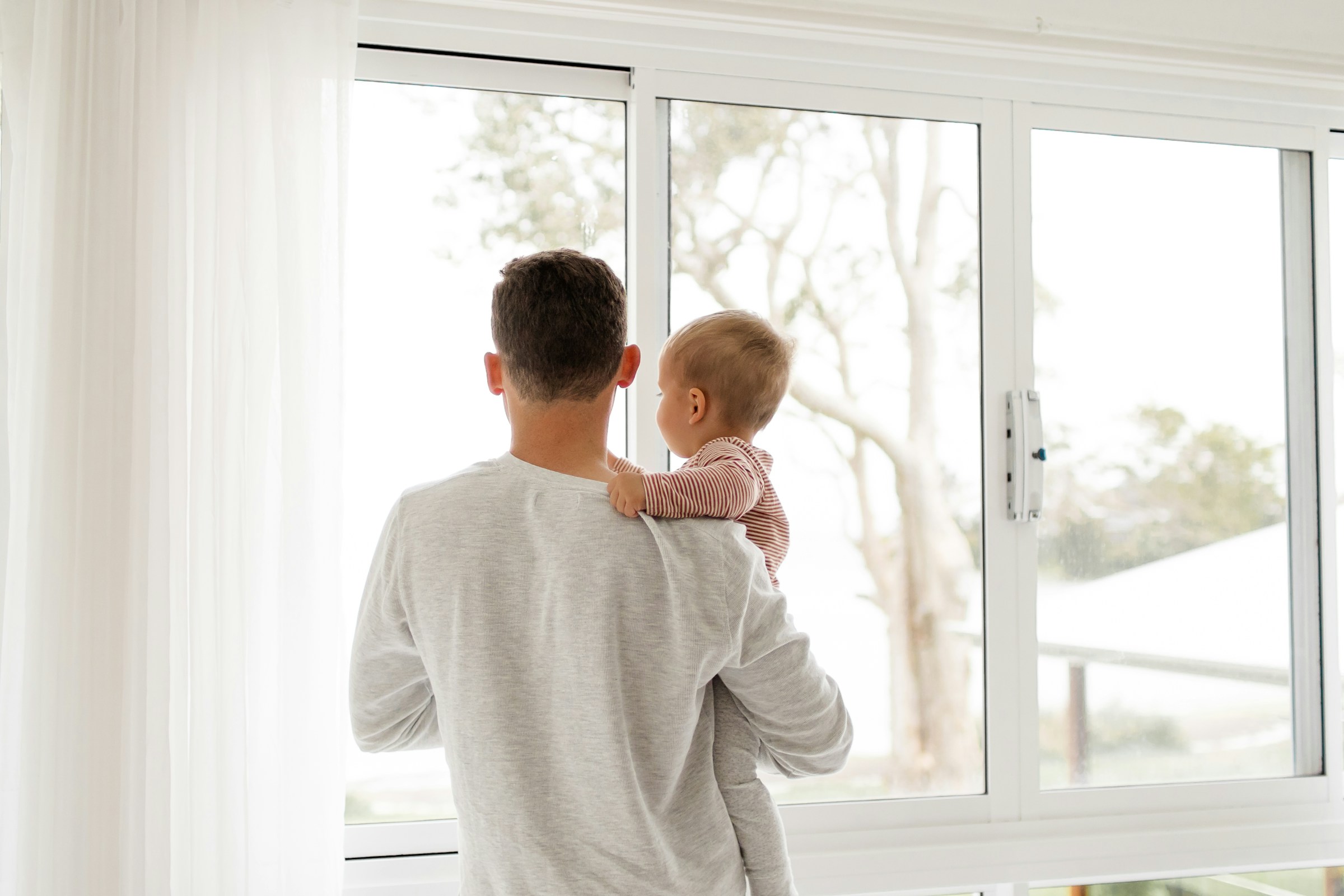 Un homme tenant un bébé qui regarde par la fenêtre | Source : Pexels
