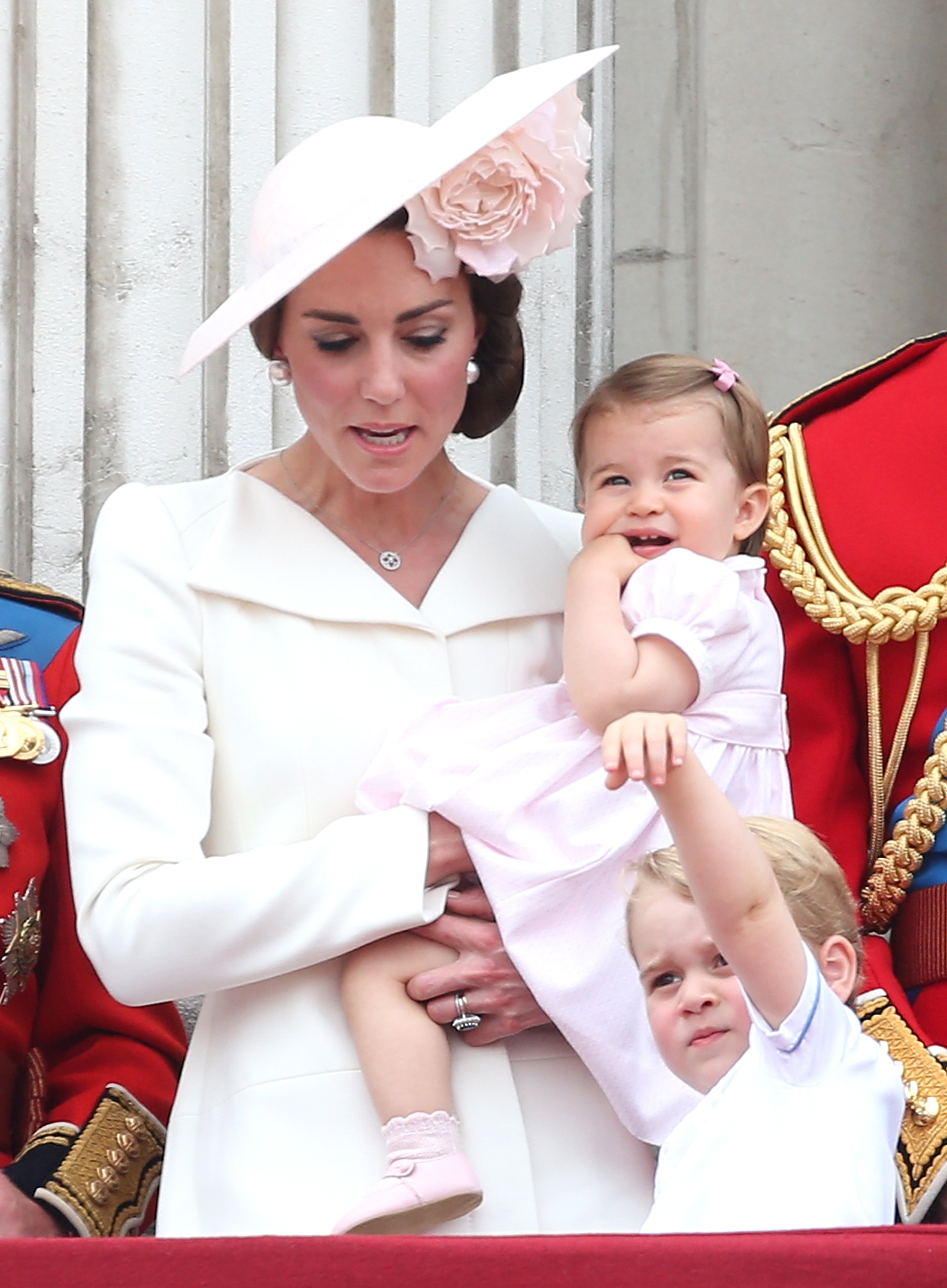 Catherine, duchesse de Cambridge, tient la petite princesse Charlotte dans ses bras, debout sur le balcon aux côtés du prince George, lors du défilé « Trooping the Colour » sur The Mall, le 11 juin 2016, à Londres, en Angleterre. Catherine est radieuse dans une robe-manteau sur mesure ivoire et un chapeau Philip Treacy rose pâle orné d'une grande fleur, tandis que Charlotte porte une robe rose pastel à manches bouffantes avec des chaussures assorties et que George tend les bras vers le haut dans un ensemble blanc à col. | Source : Getty Images