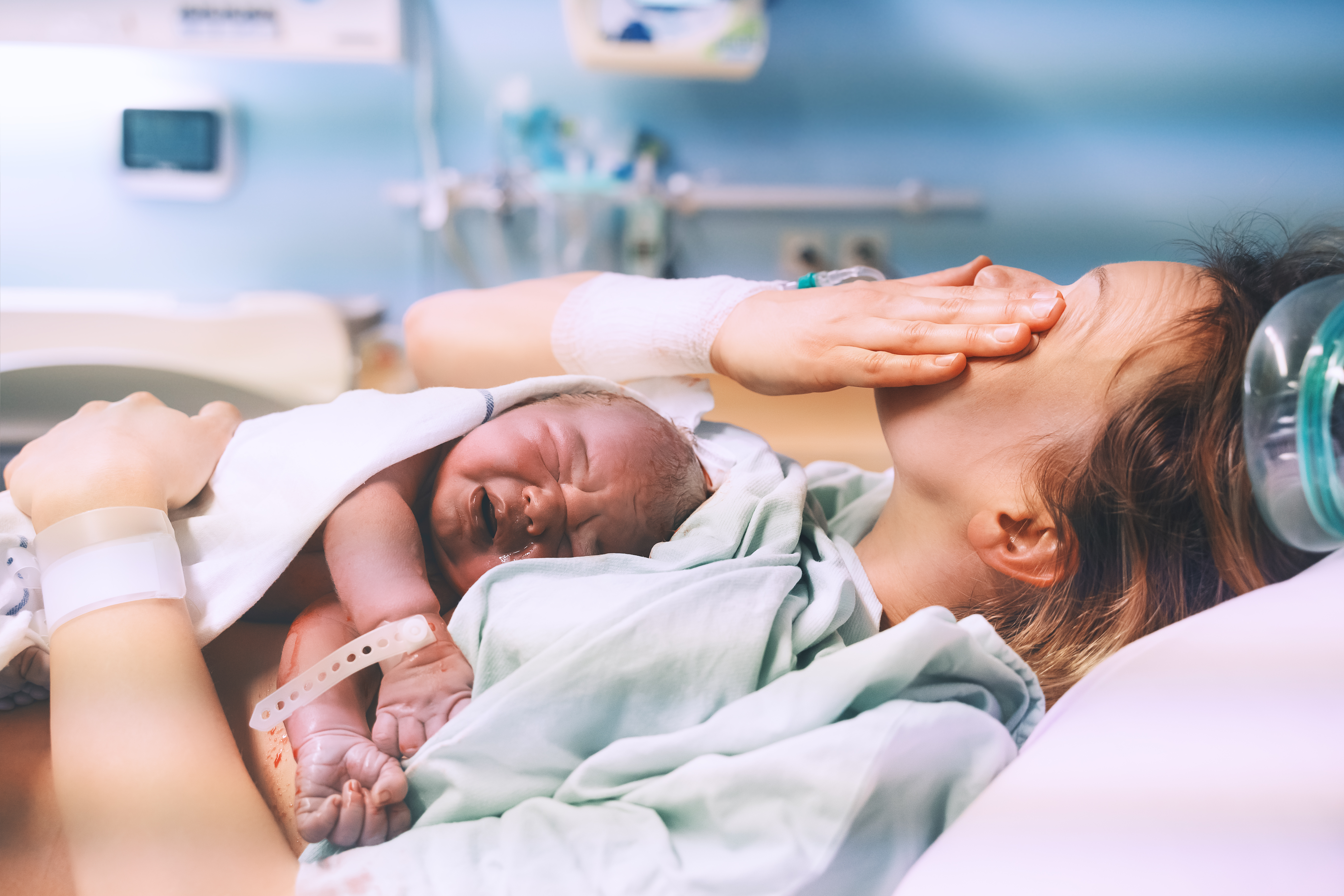 Une jeune mère essuie ses larmes tout en serrant son nouveau-né dans ses bras après l'accouchement | Source : Shutterstock