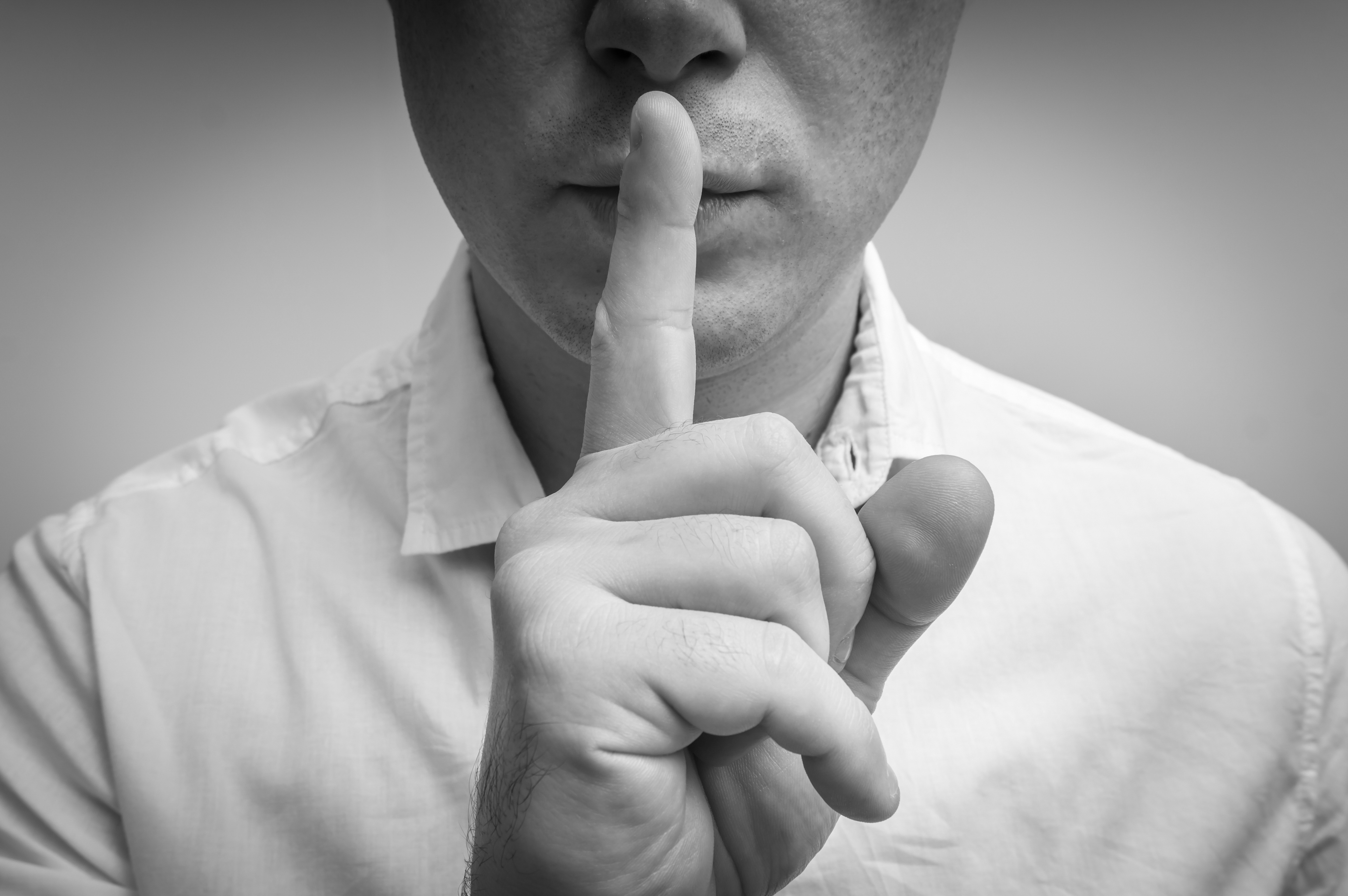 Un hombre con un dedo en los labios | Fuente: Shutterstock