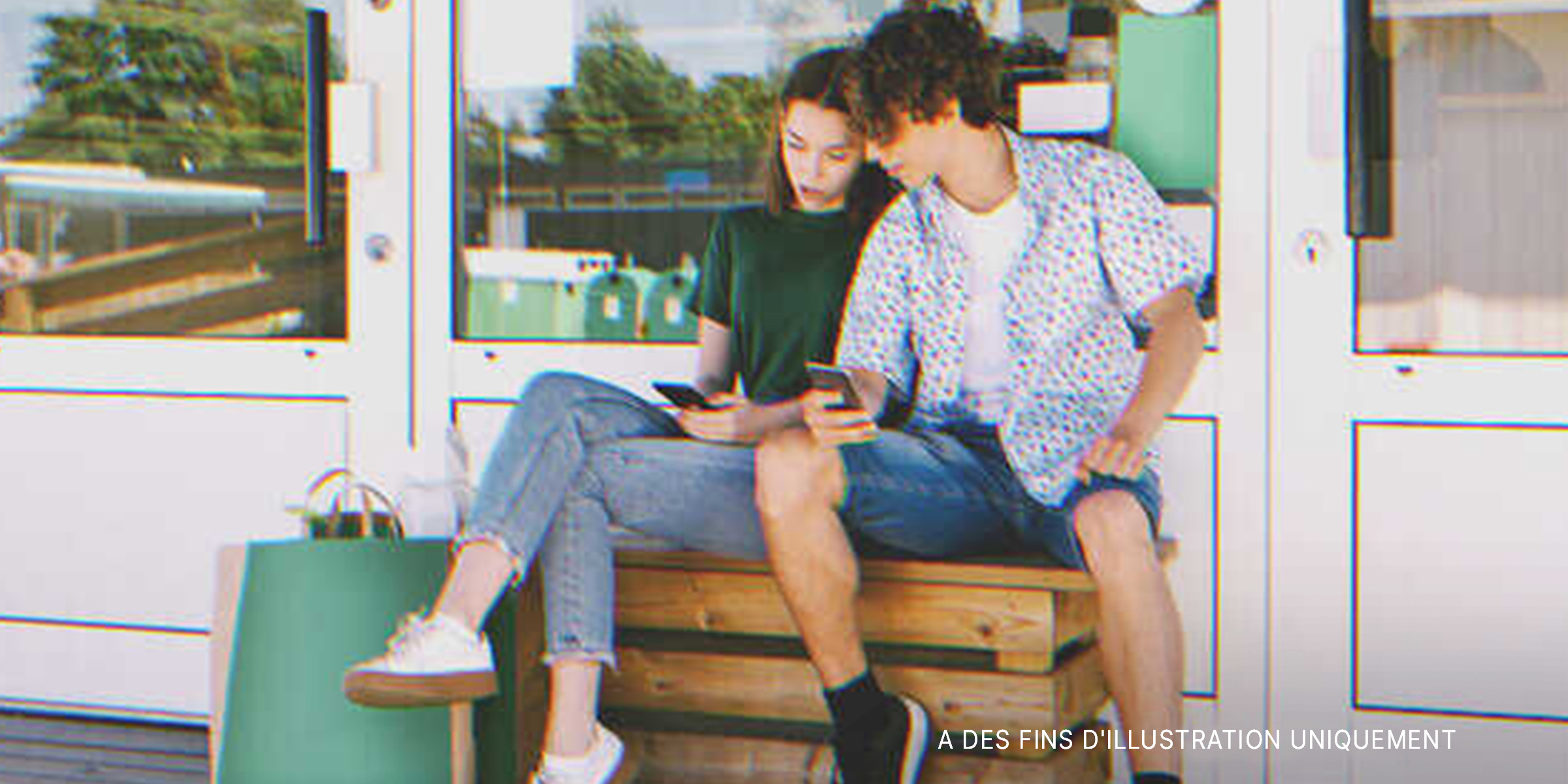 Un garçon et une fille assis à l'extérieur et regardant l'écran d'un téléphone | Source : Shutterstock