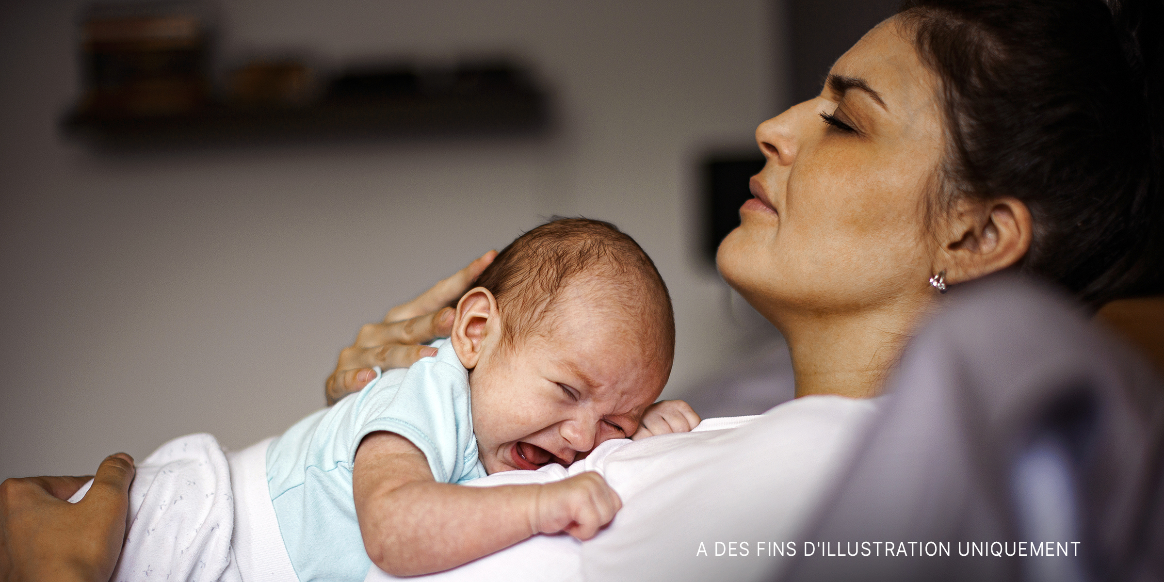 Une femme en détresse allongée avec son bébé en pleurs sur la poitrine | Source : Getty Images