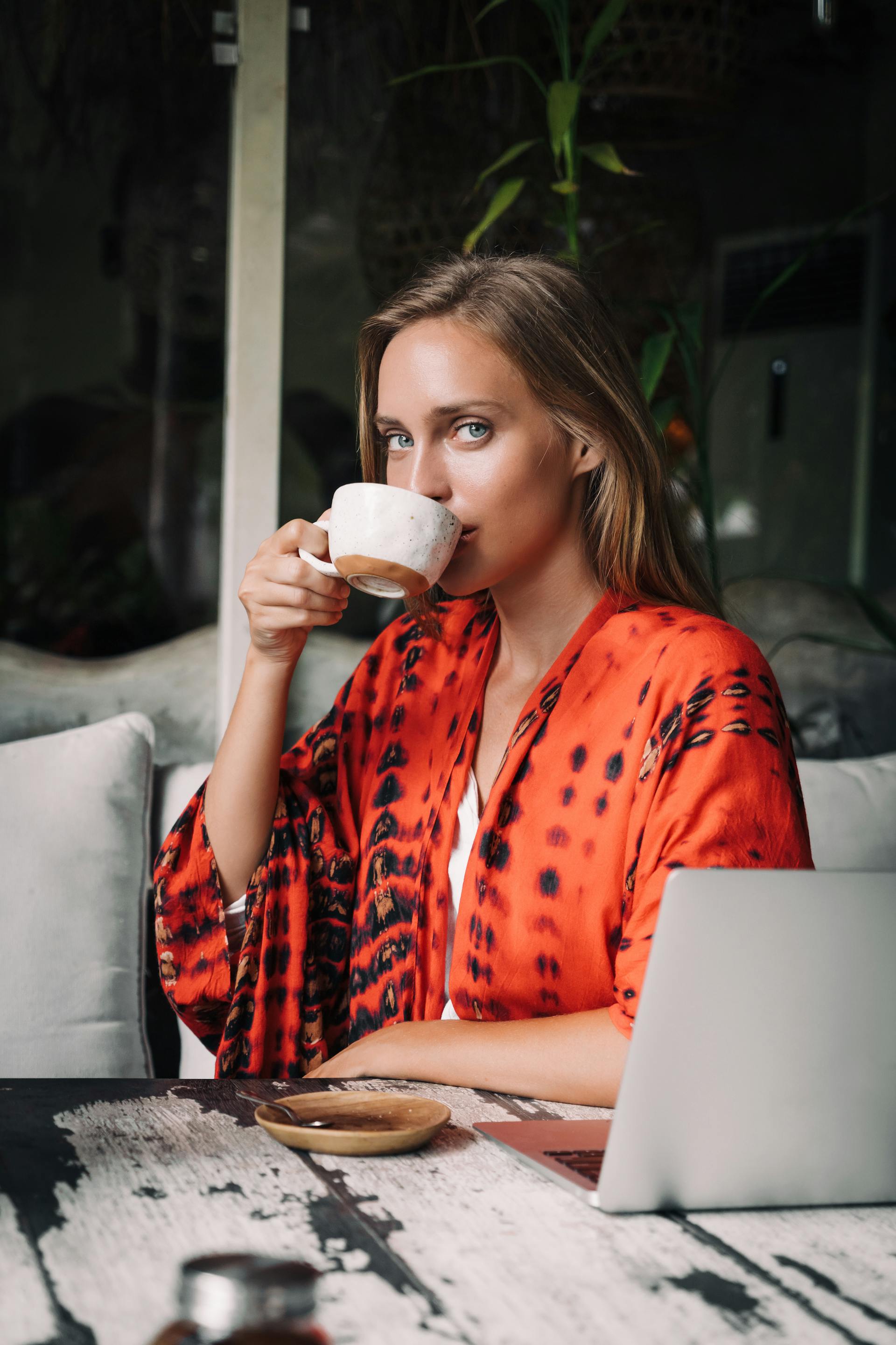 Une femme qui boit un café avec son ordinateur portable devant elle | Source : Pexels