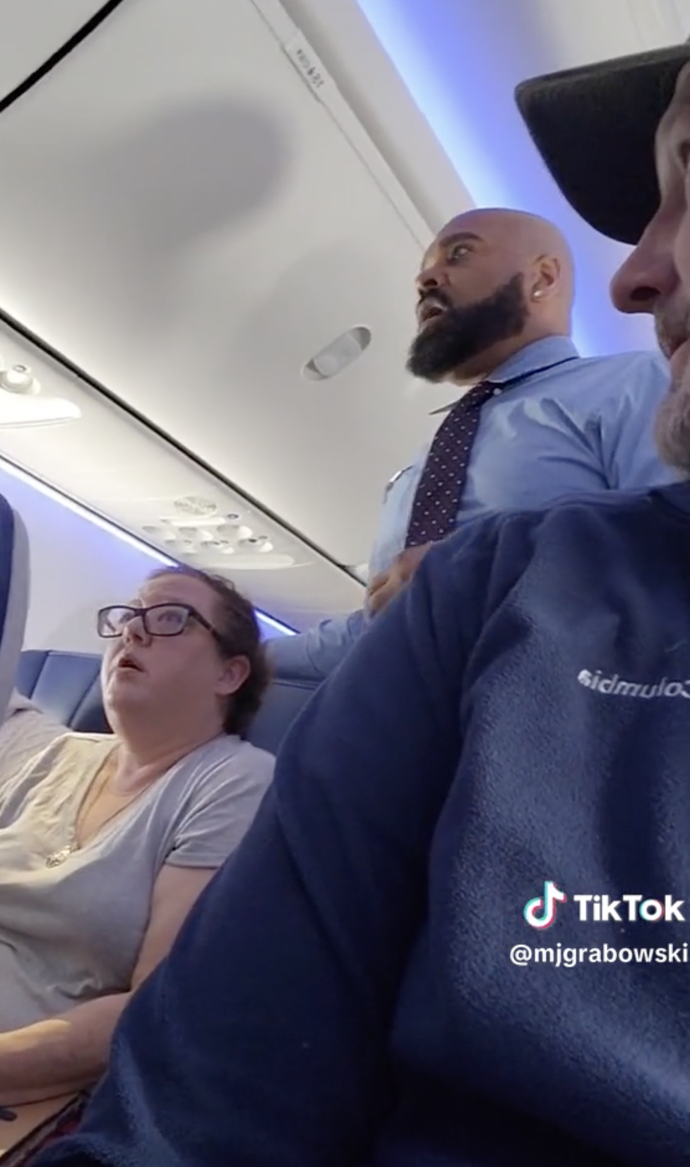 Un homme s'amuse à enregistrer un passager irrité qui se plaint des pleurs d'un bébé à bord d’un vol de Southwest Airlines, tandis que le personnel de bord tente de le calmer. La passagère à côté de l'homme en colère est visible sur le cliché | Source : TikTok/mjgrabowski