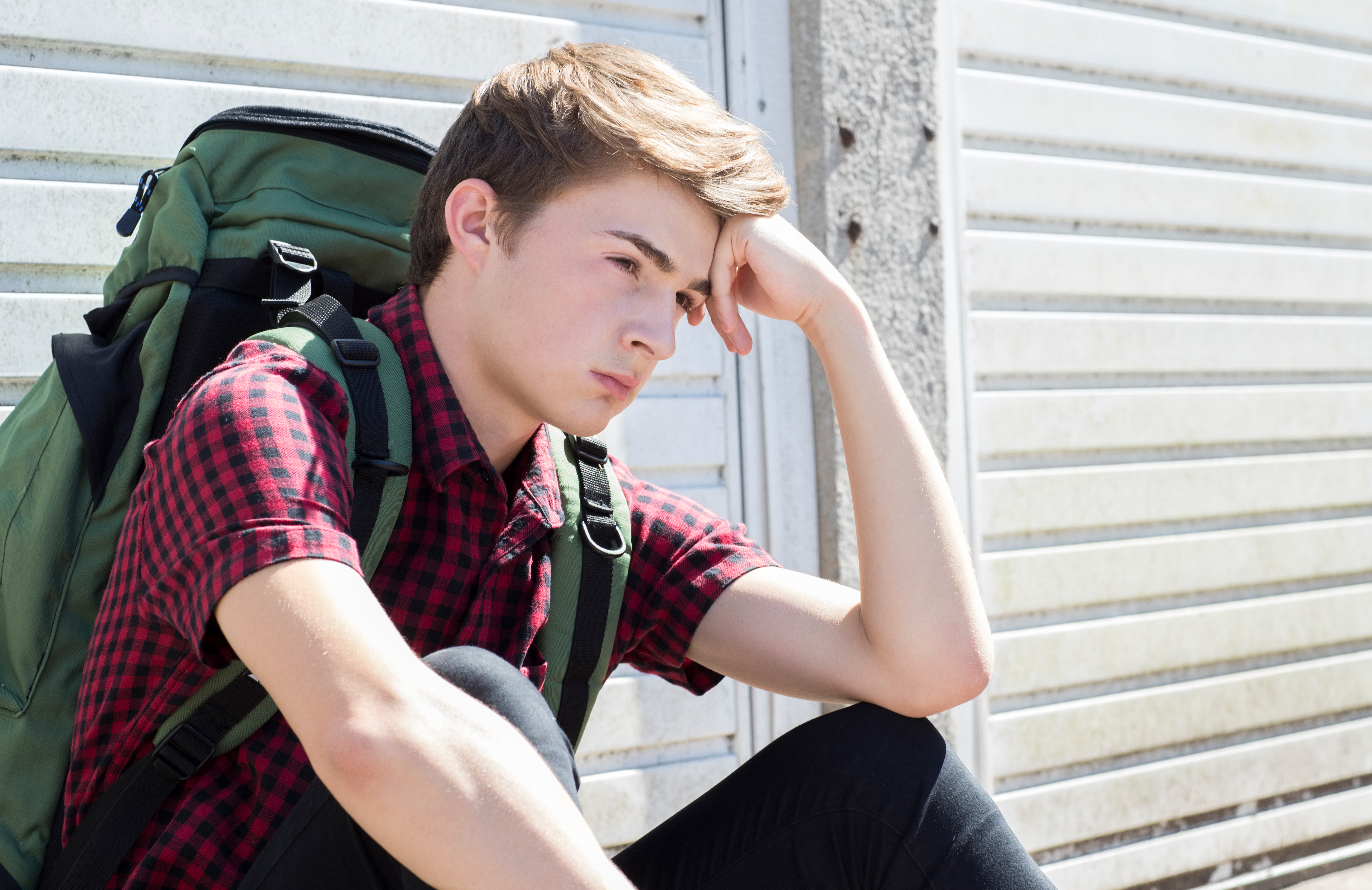 Un adolescent à l'air stressé avec un sac à dos assis dans la rue | Source : Shutterstock