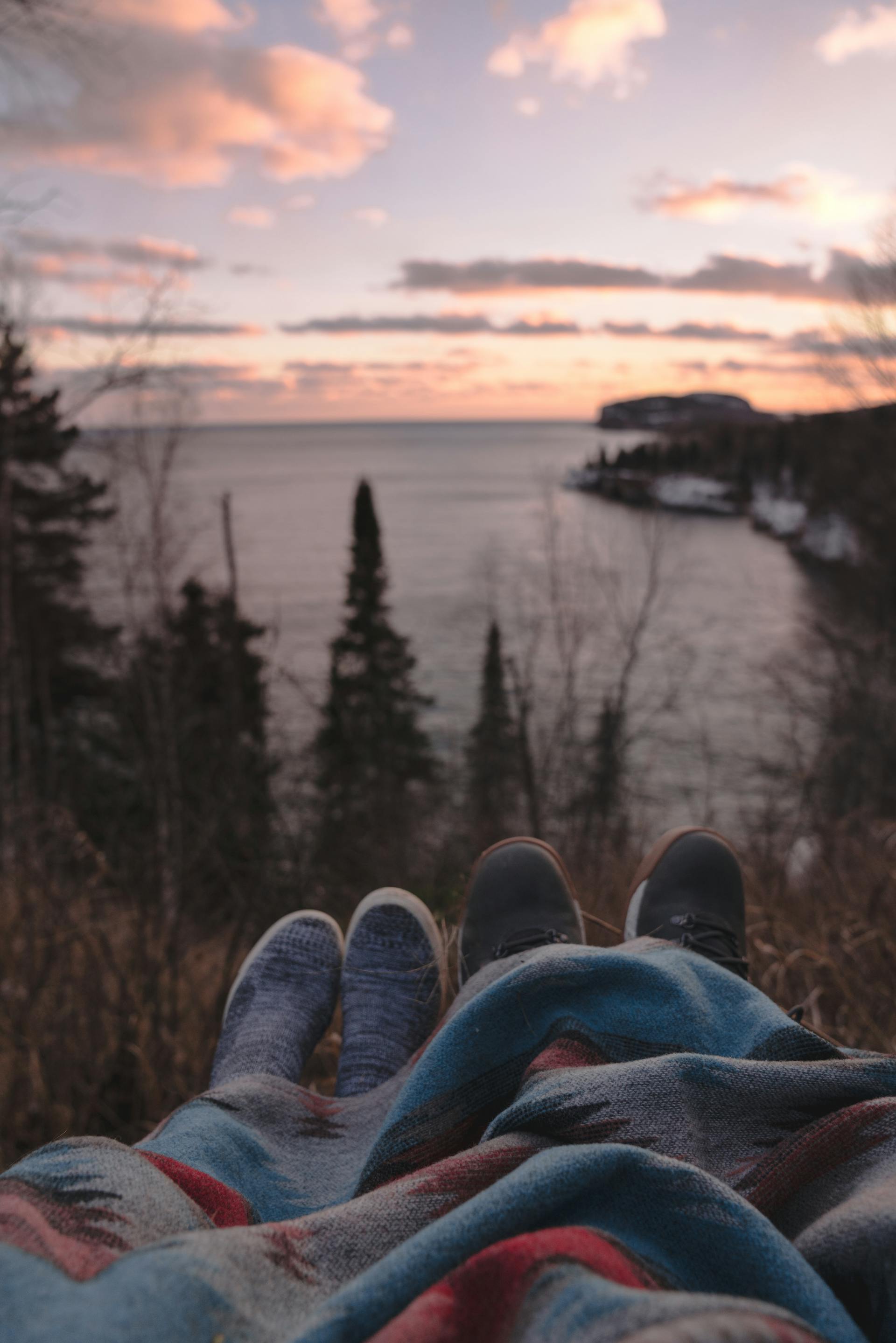 Un couple anonyme allongé sur une colline au bord de la mer et profitant du coucher de soleil | Source : Pexels