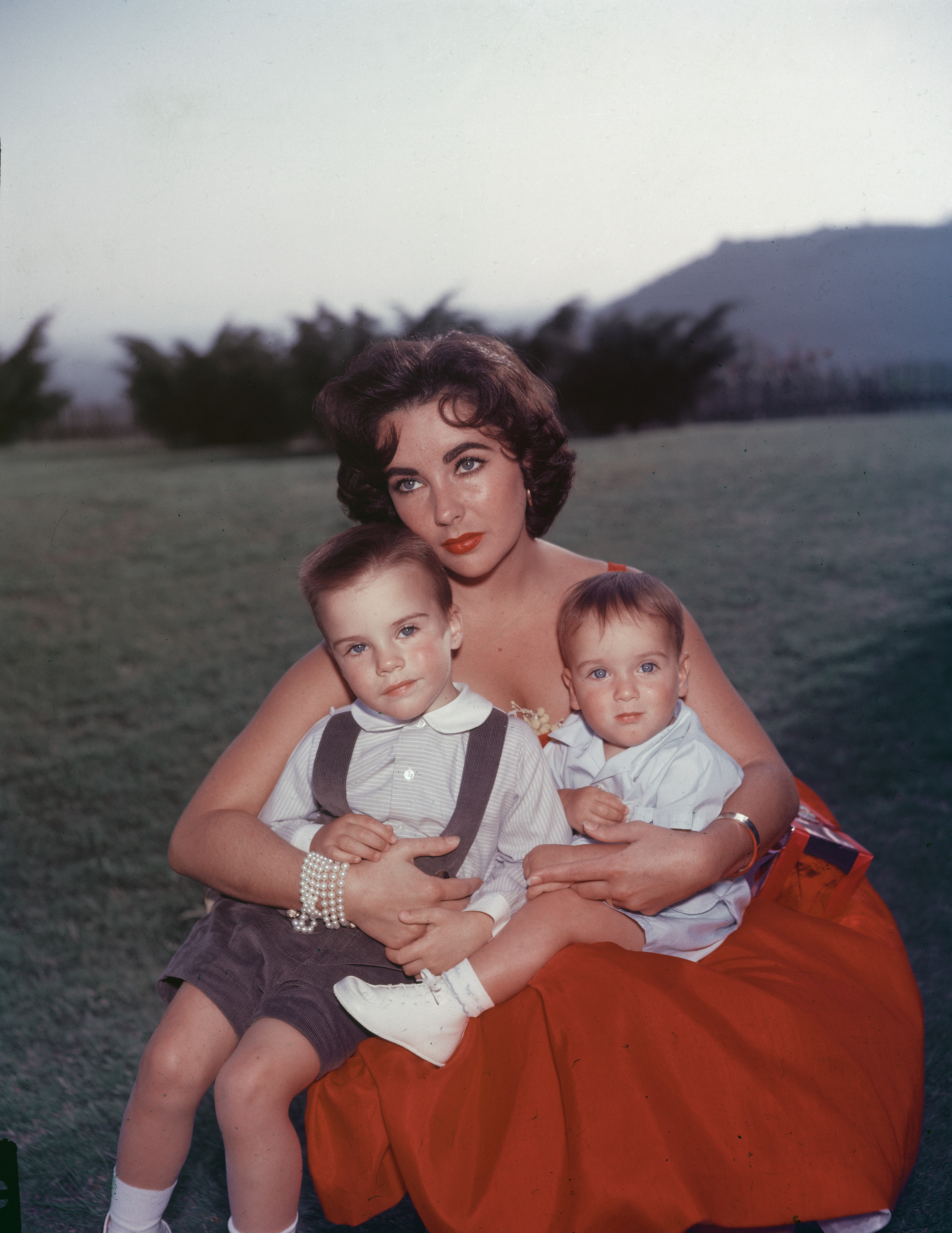 Elizabeth Taylor est photographiée en robe de soirée rouge avec ses fils Michael et Christopher Wilding sur ses genoux | Source : Getty Images