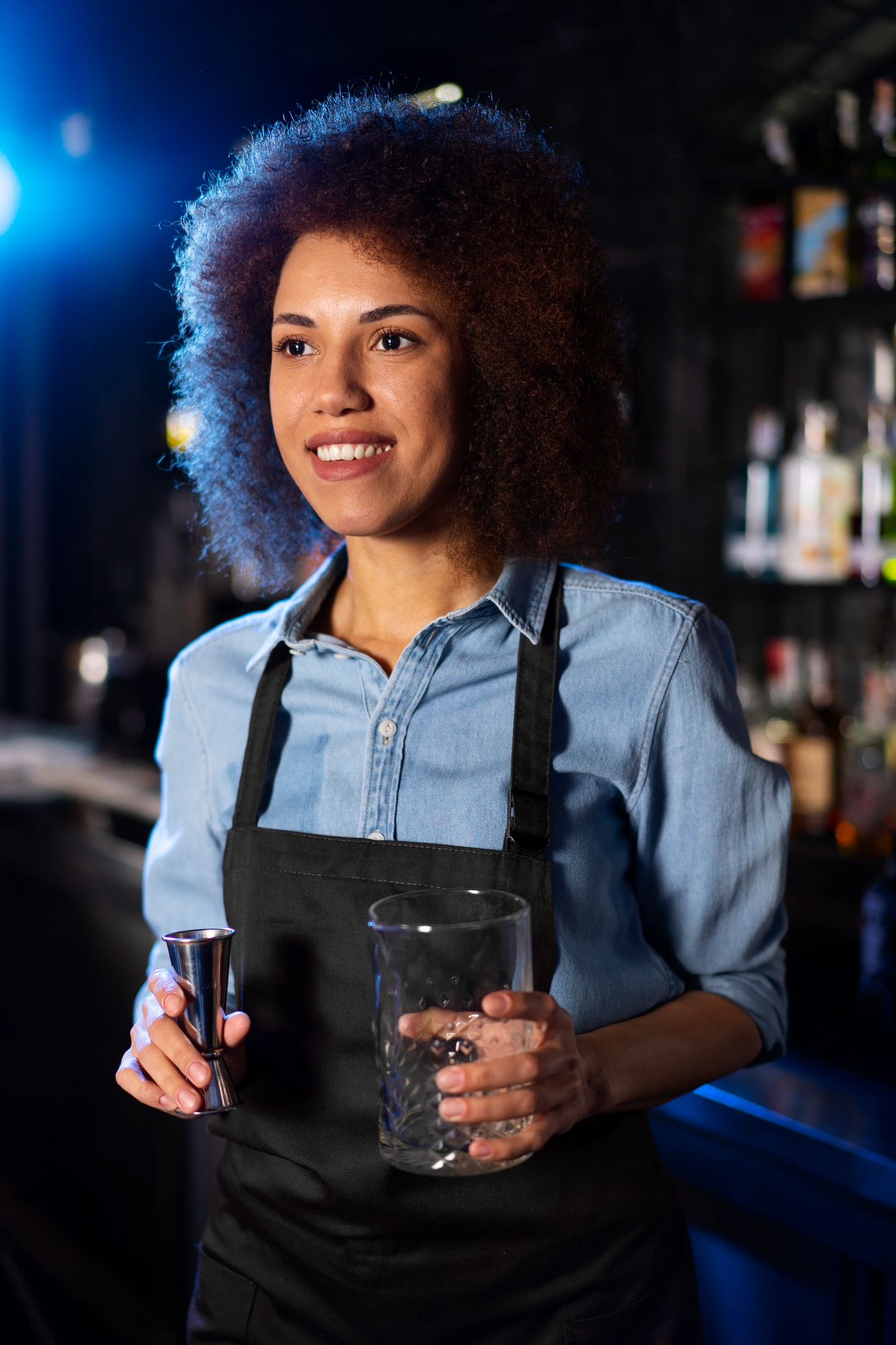 Une serveur heureuse tenant un verre et un verseur de shot pour une boisson | Source : Freepik