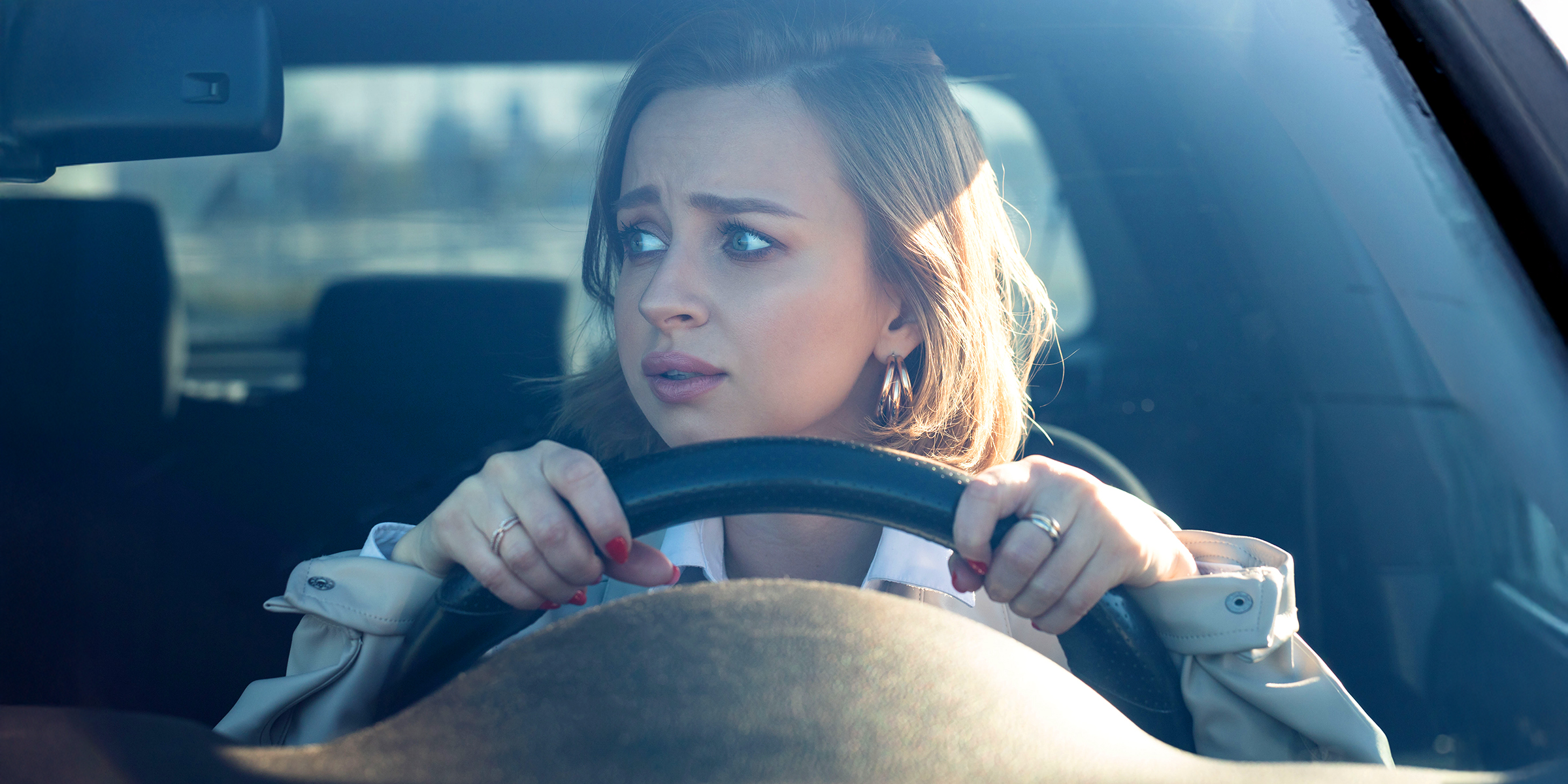 Une jeune femme agrippée au volant, regardant devant elle avec de grands yeux anxieux | Source : Shutterstock