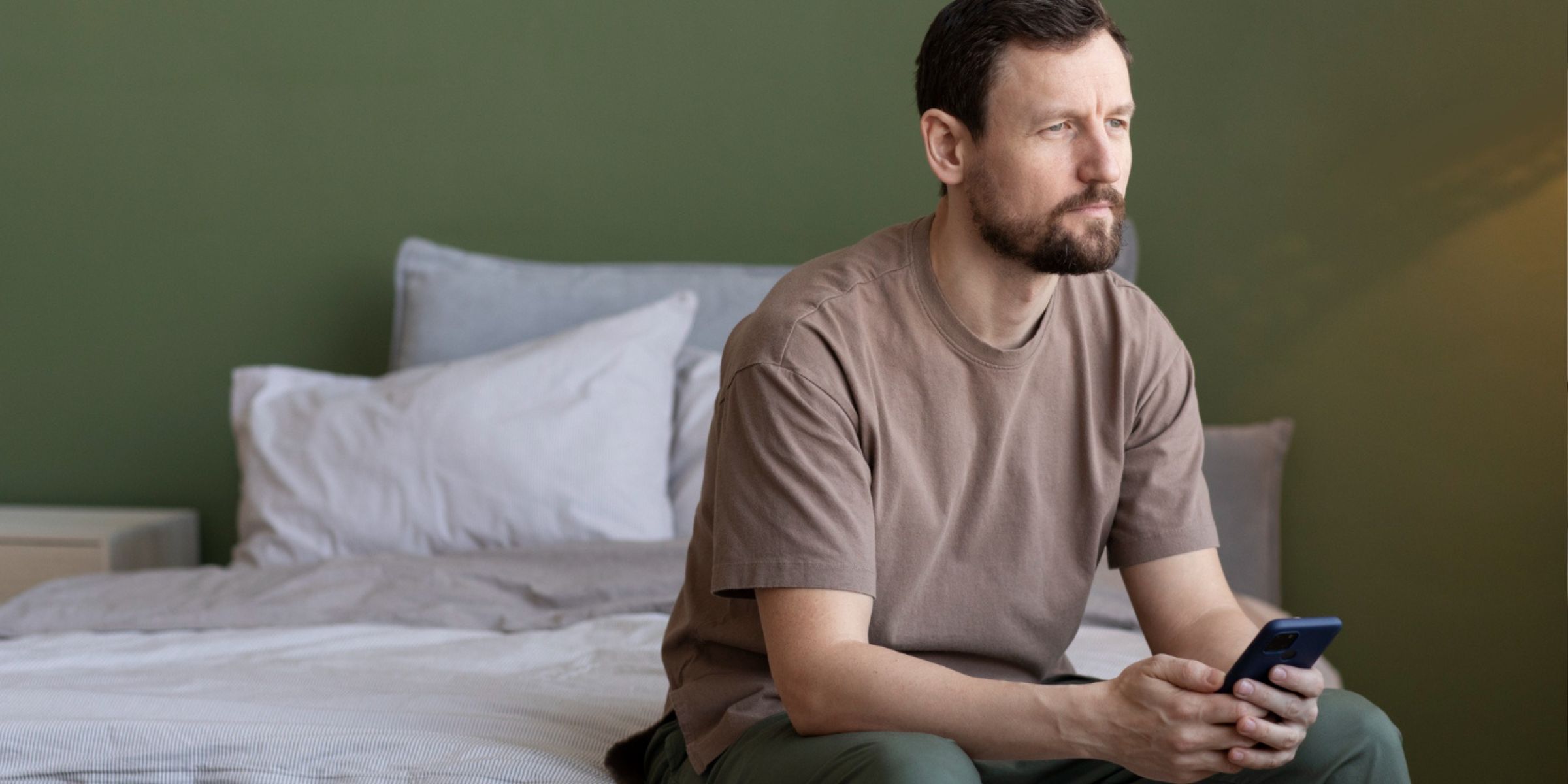 Un homme tenant son téléphone et assis sur le lit | Source : Freepik