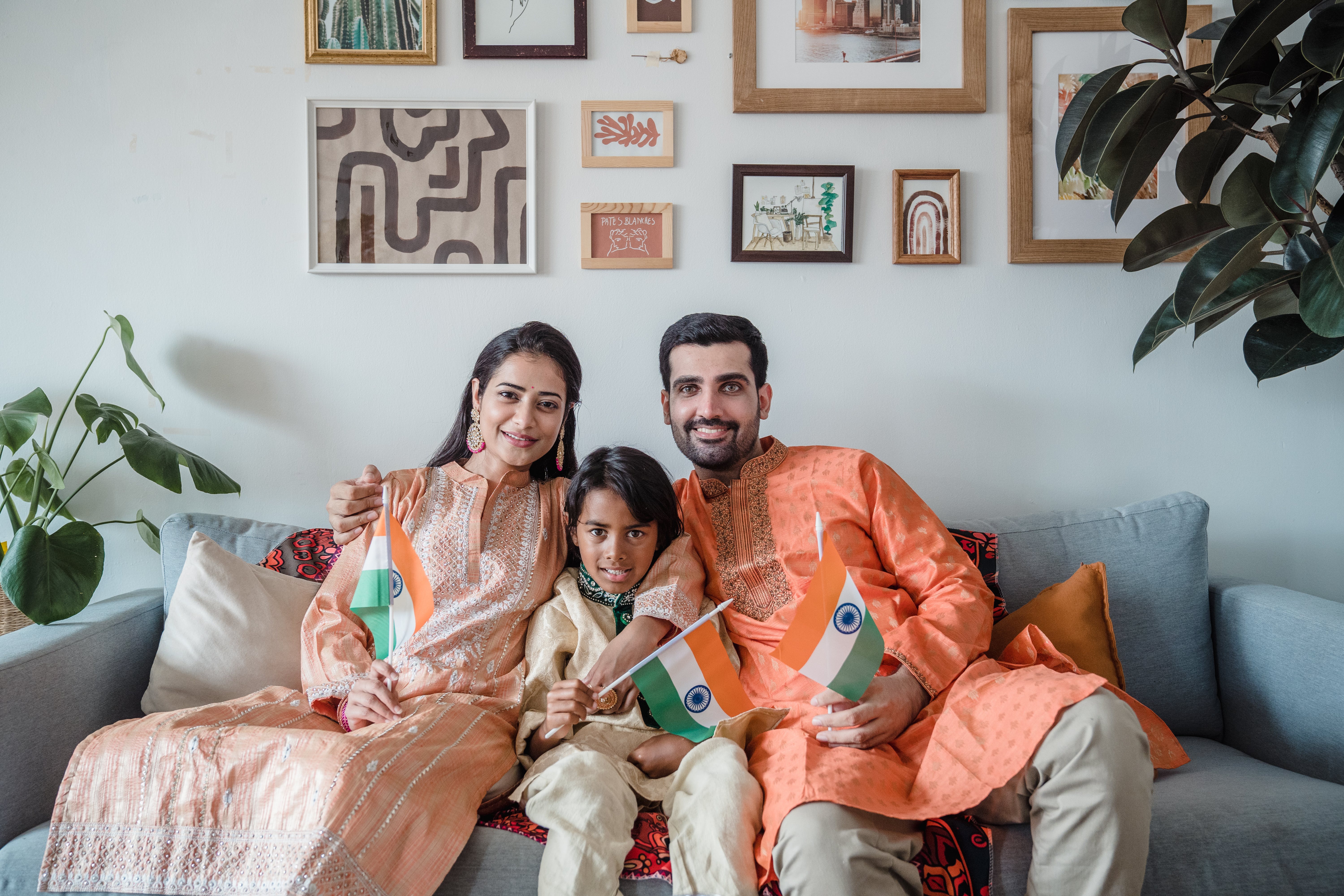 Une famille heureuse de trois personnes assises sur un canapé et tenant le drapeau de leur pays | Source : Pexels