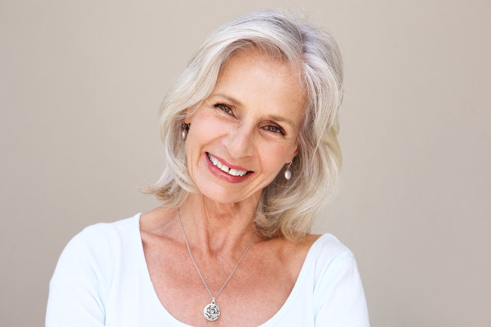 Une belle femme âgée souriante et debout au mur | Source : Shutterstock