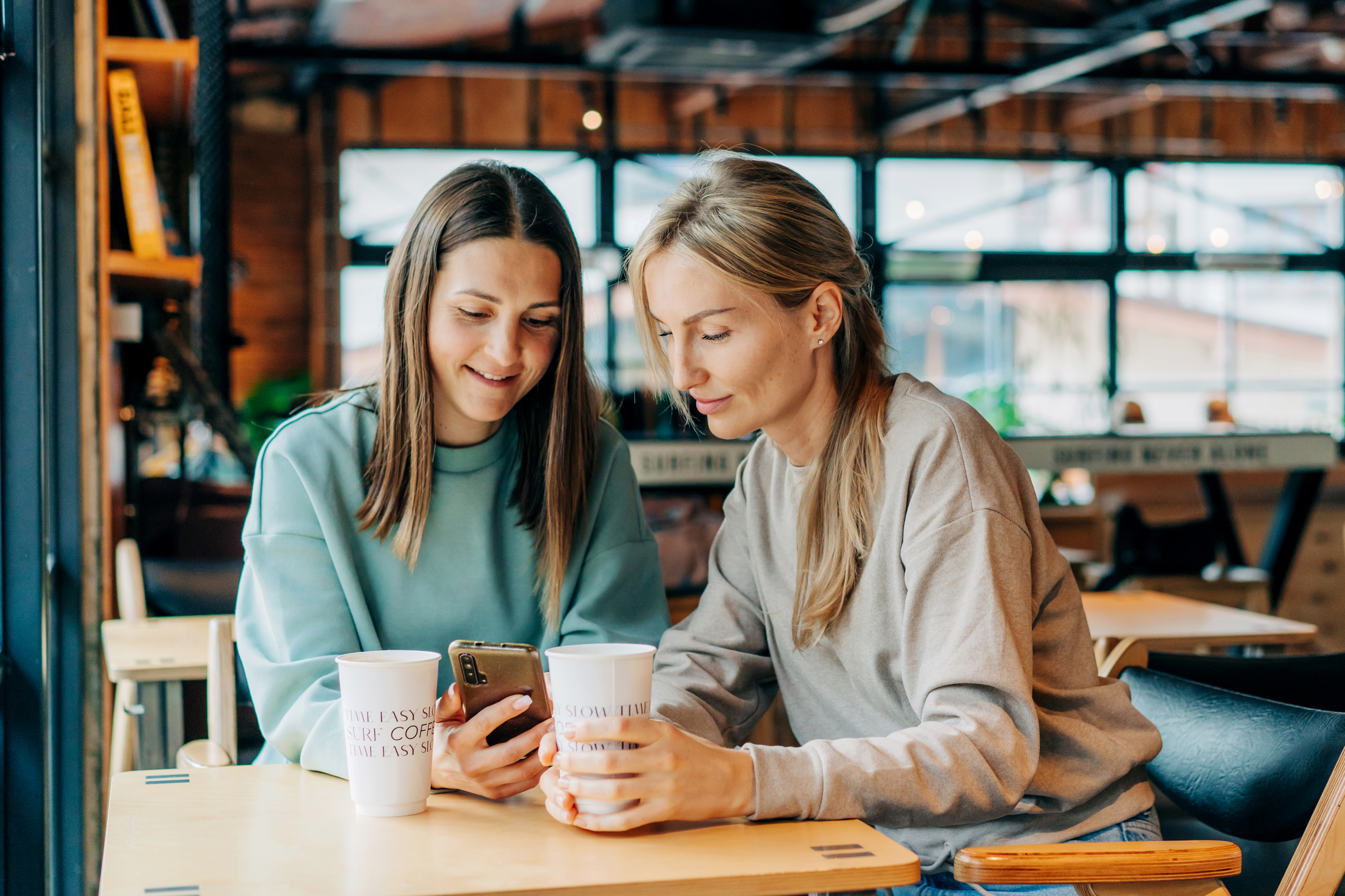 Deux femmes souriantes et joyeuses regardent les réseaux sociaux dans un téléphone portable | Source : Getty Images