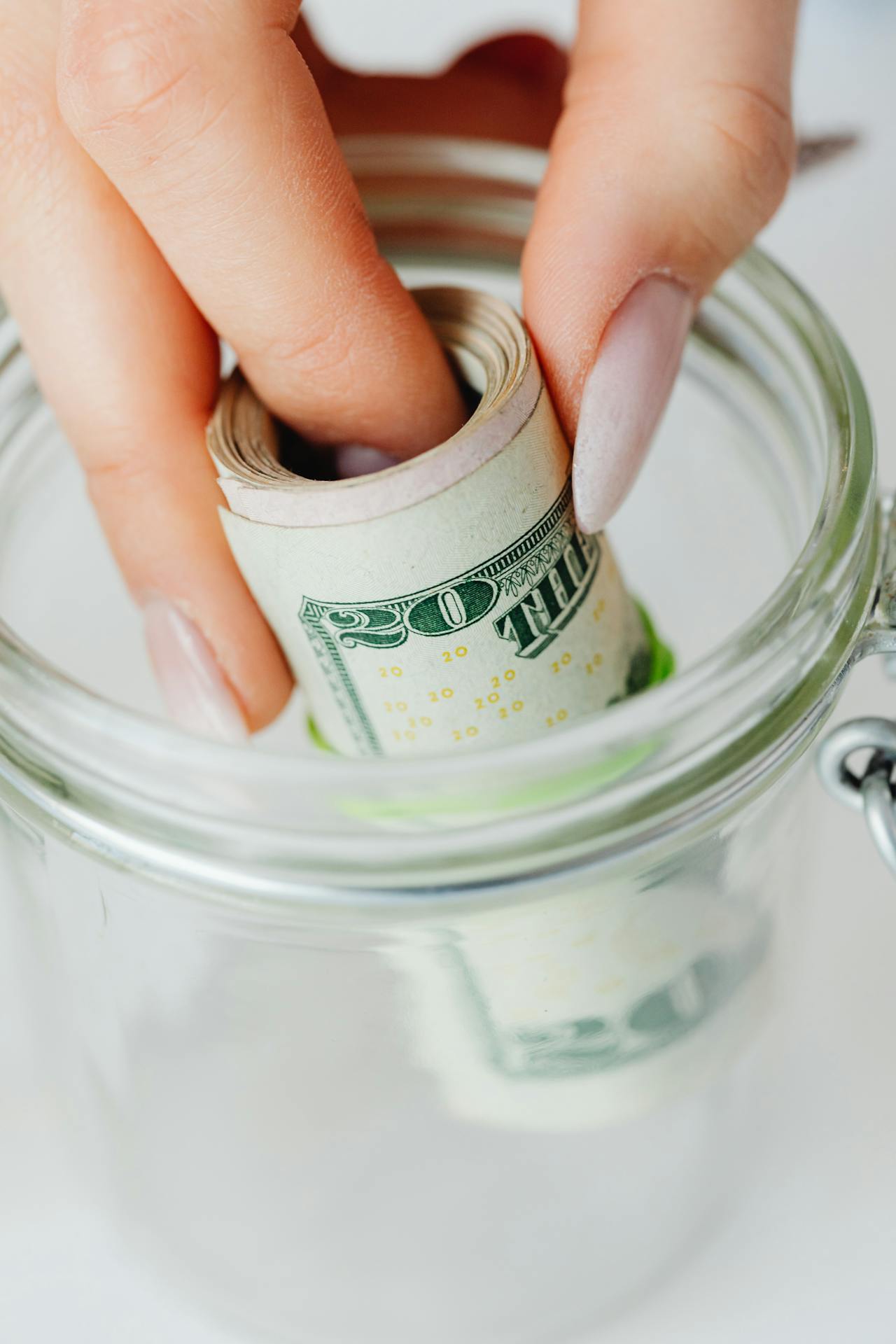 Une femme mettant des billets de banque roulés dans un bocal en verre | Source : Pexels