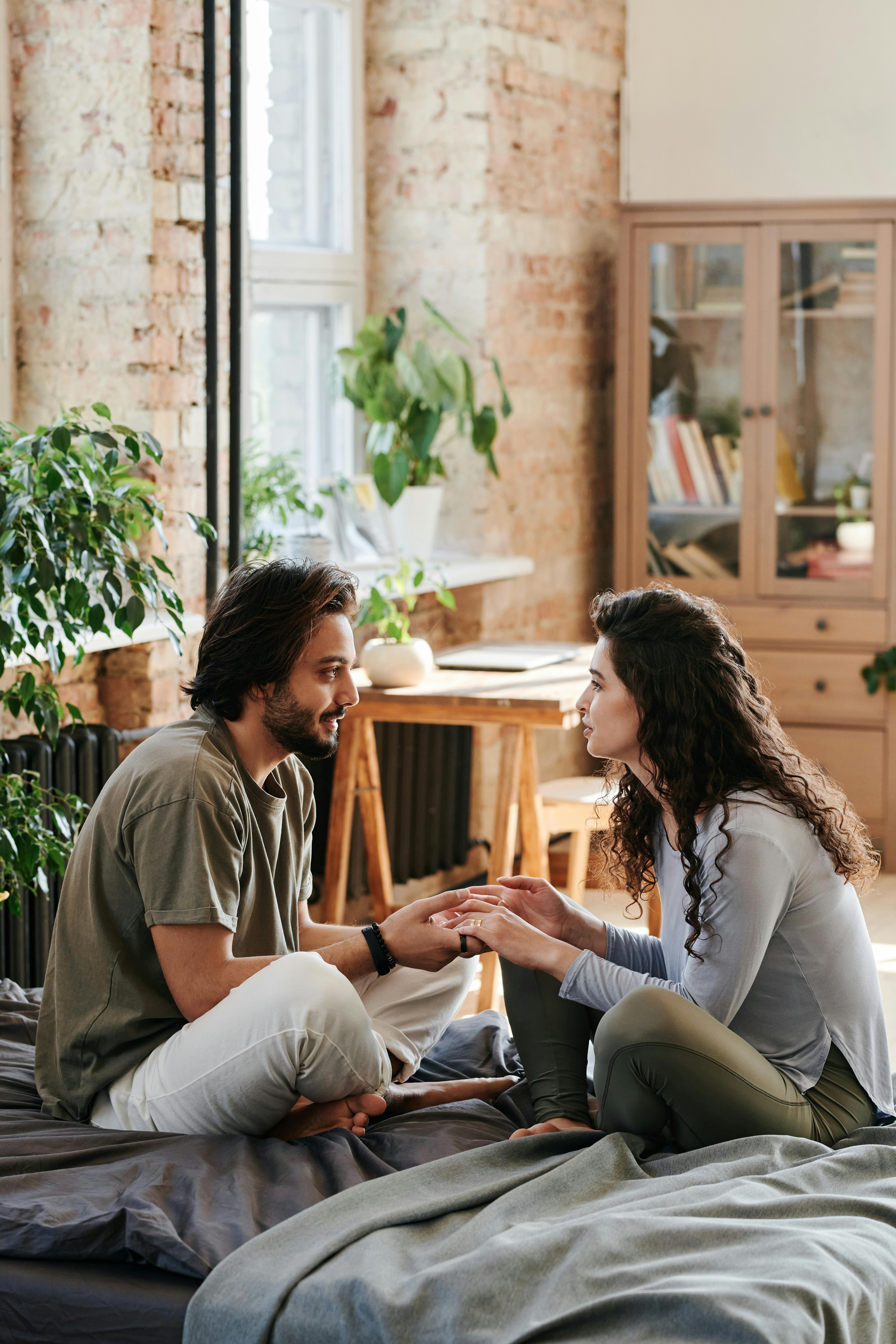 Homme tenant les mains d'une femme alors qu'ils se regardent assis sur un lit | Source : Pexels