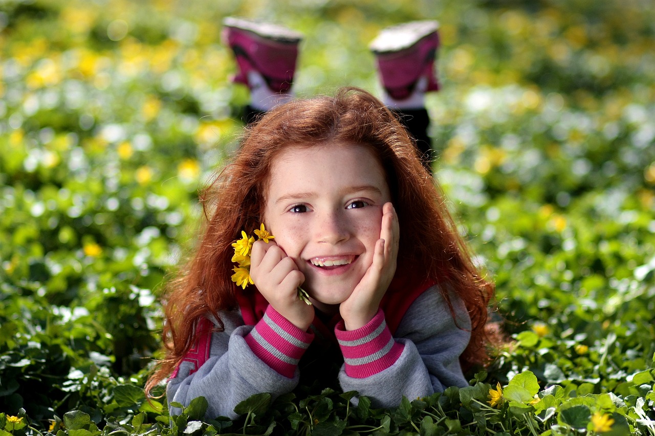 Une jeune fille rousse souriante tenant des fleurs | Source : Pixabay