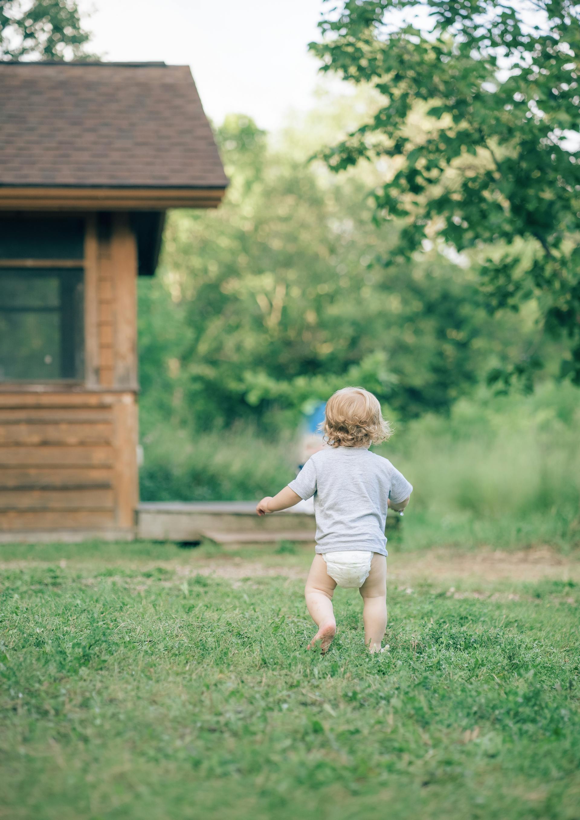 Vue de dos d'un bambin en couche qui court dans le jardin | Source : Pexels