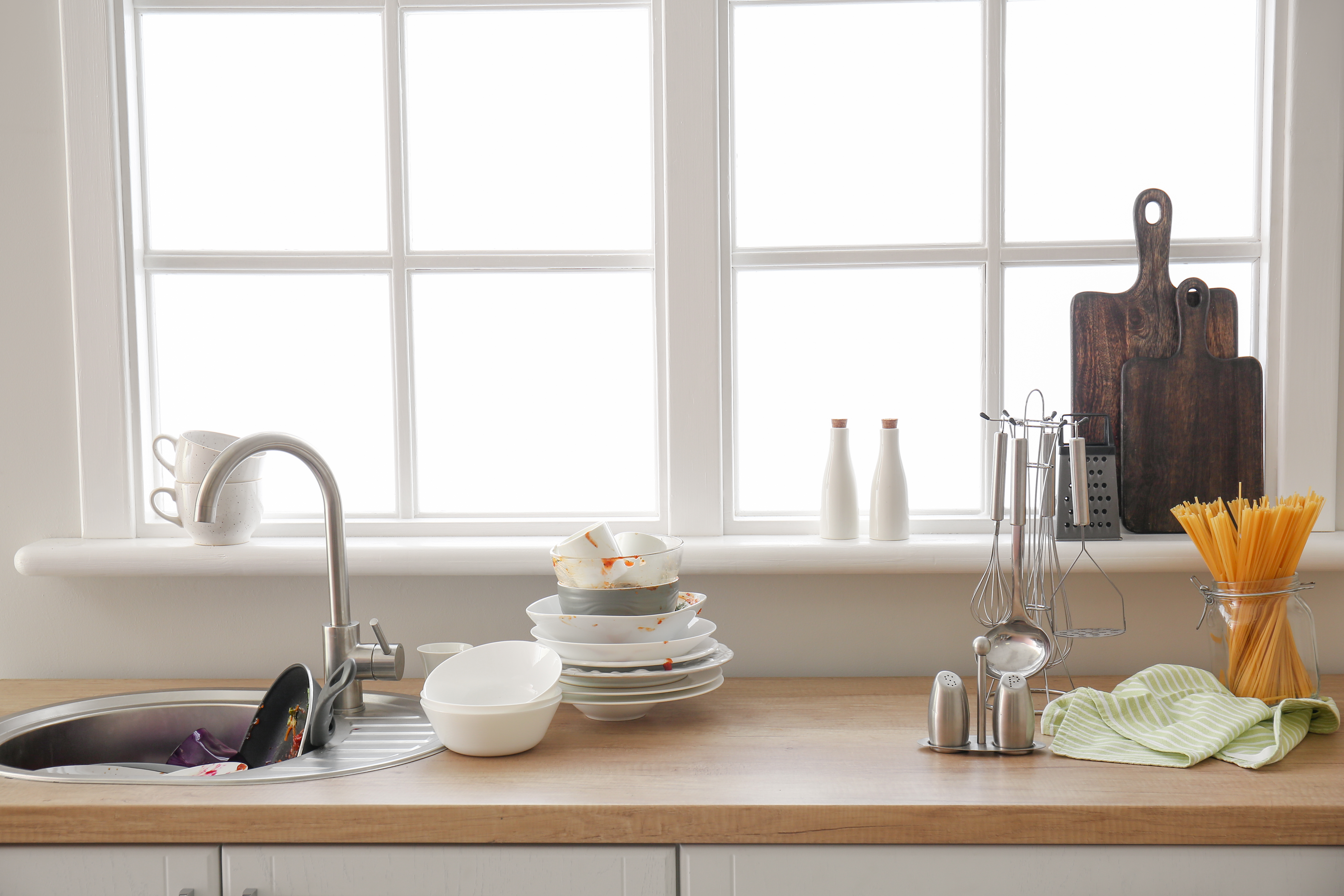 Vaisselle sale empilée à côté d'un évier de cuisine | Source : Shutterstock