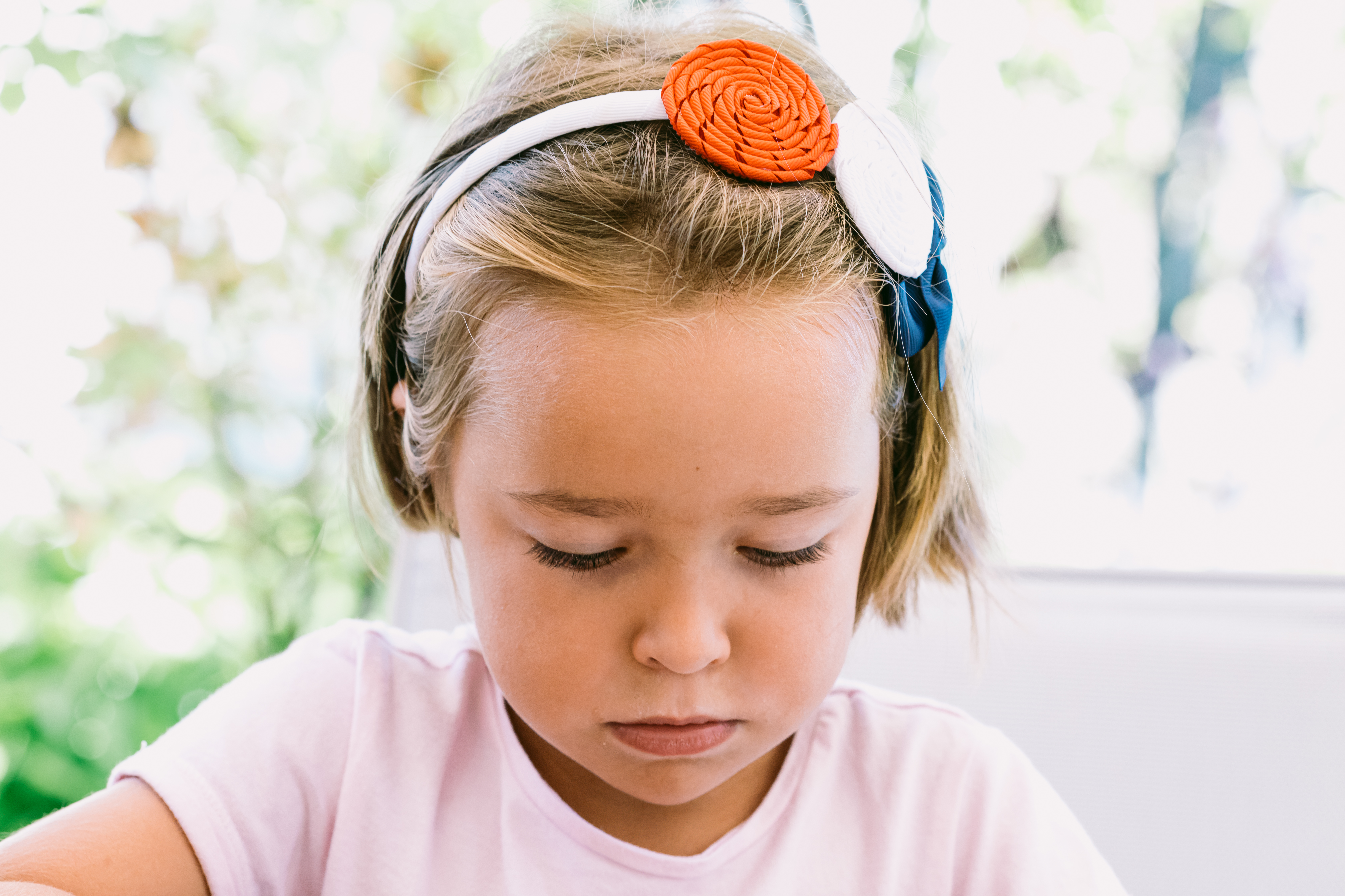 Portrait d'une petite fille sérieuse aux cheveux blonds, portant un bandeau blanc avec des décorations bleues, rouges et blanches, avec un jardin en arrière-plan | Source : Getty Images