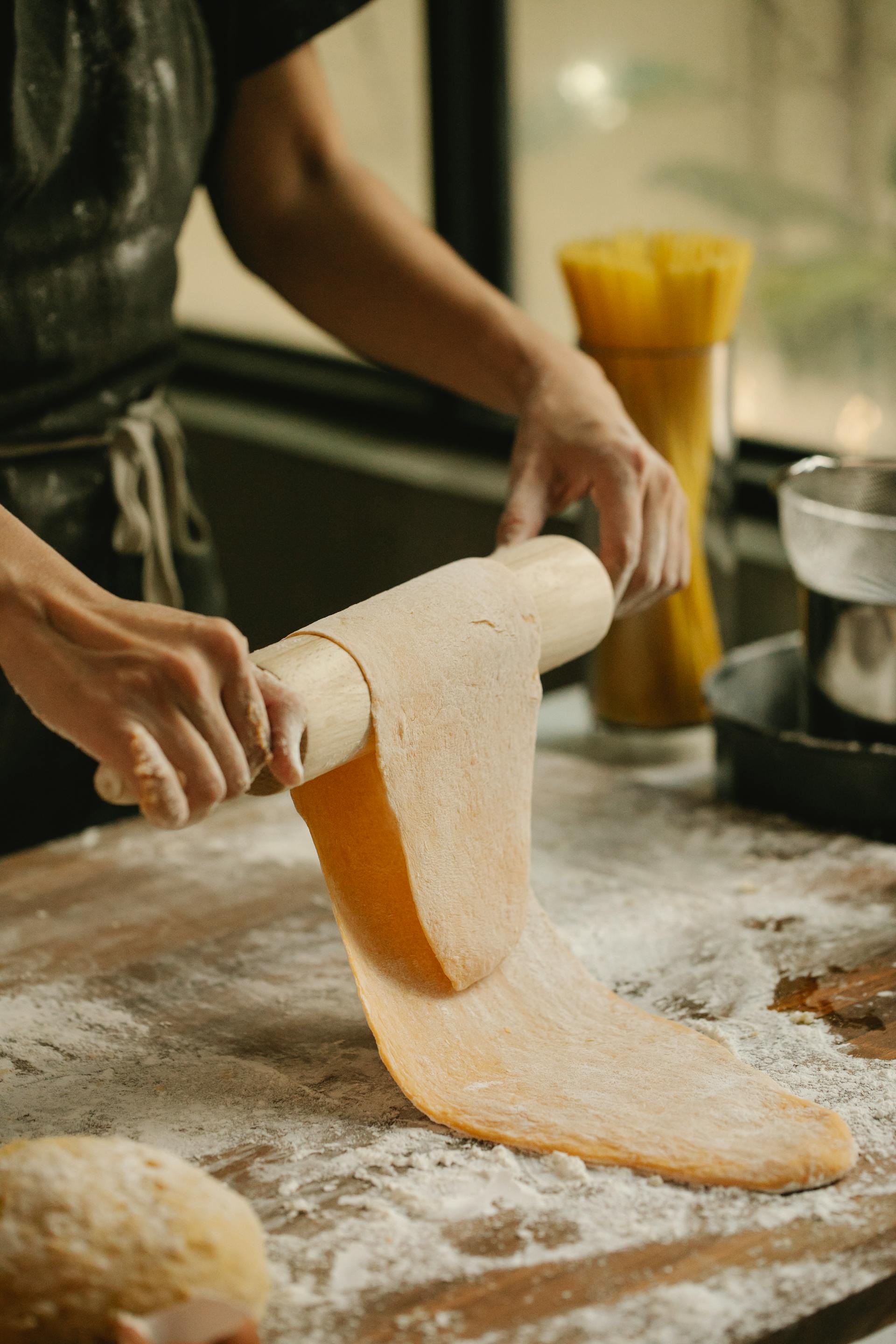 Gros plan sur une jeune femme qui roule de la pâte sur une table farineuse à la maison | Source : Pexels