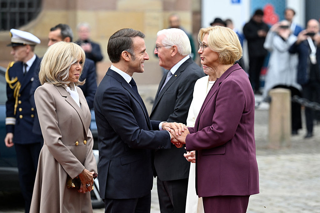 Le président français Emmanuel Macron (2e à g.) et son épouse Brigitte Macron (à g.) sont accueillis par la ministre-présidente du Land de Sarre, Anke Rehlinger, devant la Chancellerie d'État de Sarre, lors des célébrations du 3 octobre 2025, jour de l'unité allemande, à Sarrebruck, dans le sud-ouest de l'Allemagne. Ce 3 octobre 2025, l'Allemagne célèbre le 35e anniversaire de la réunification allemande. | Source : Getty Images