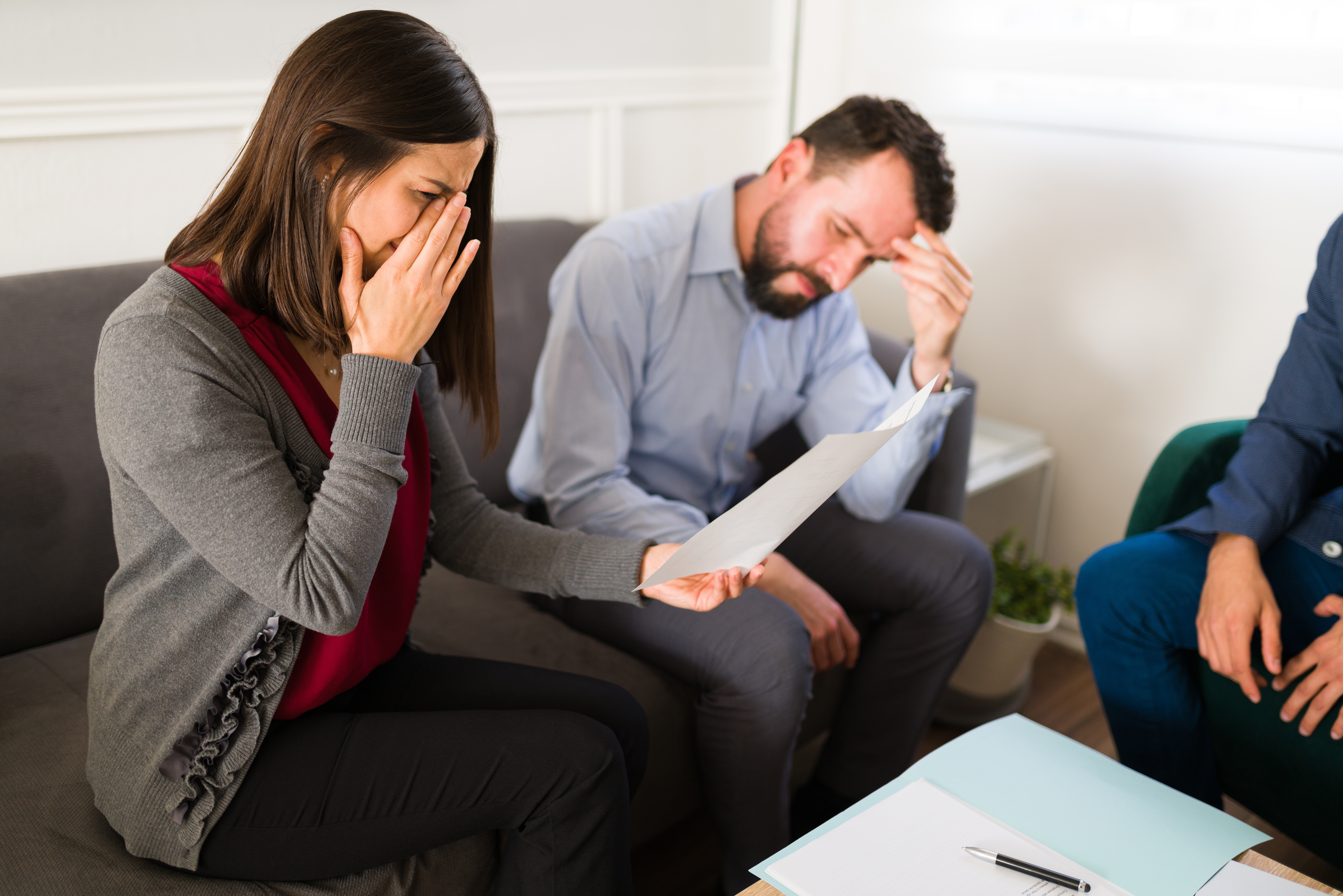 Une femme qui pleure en tenant un morceau de papier dans sa main avec un homme assis à côté d'elle | Source : Shutterstock