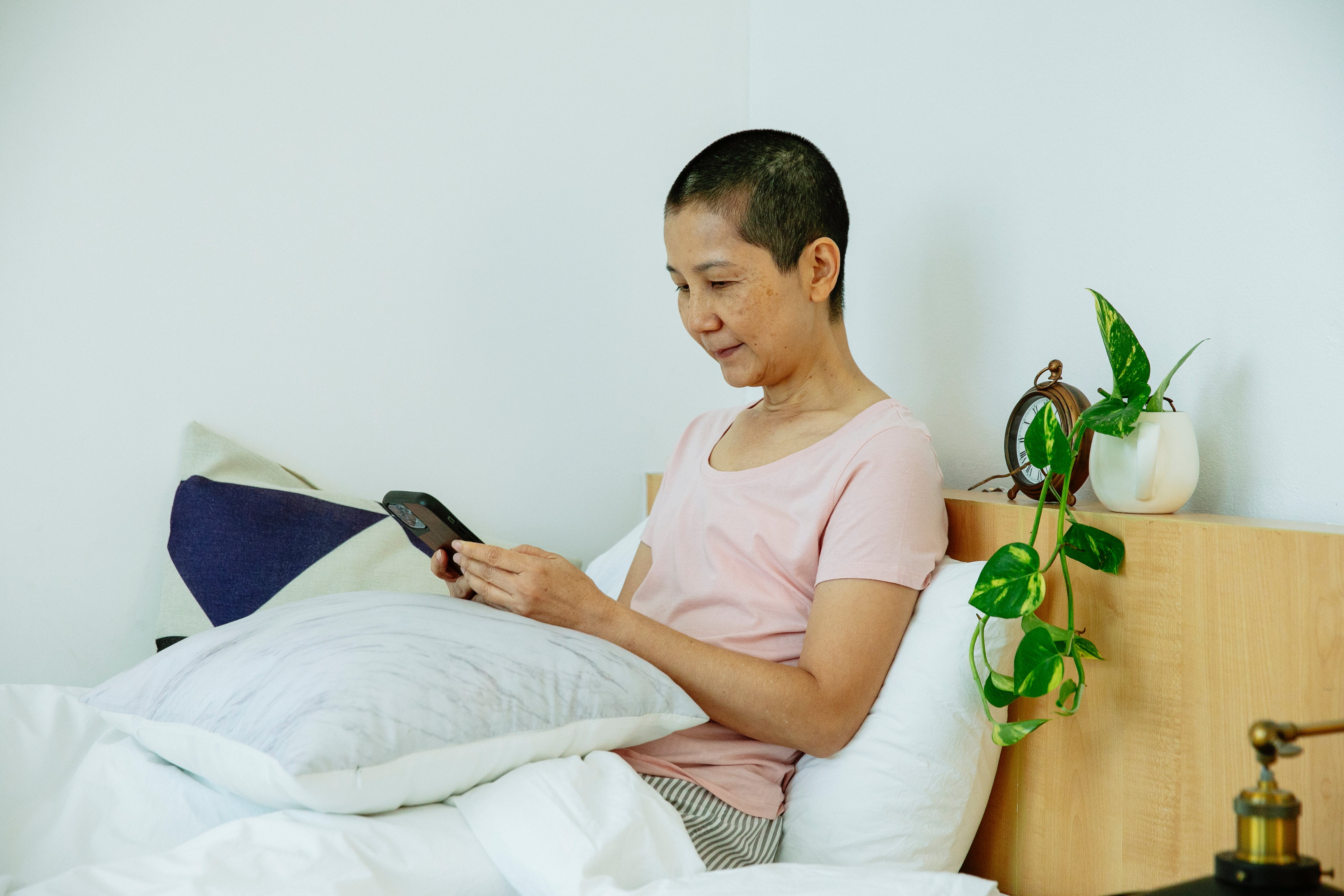 Une femme utilisant un smartphone alors qu'elle est sur le lit┃Source : Pexels