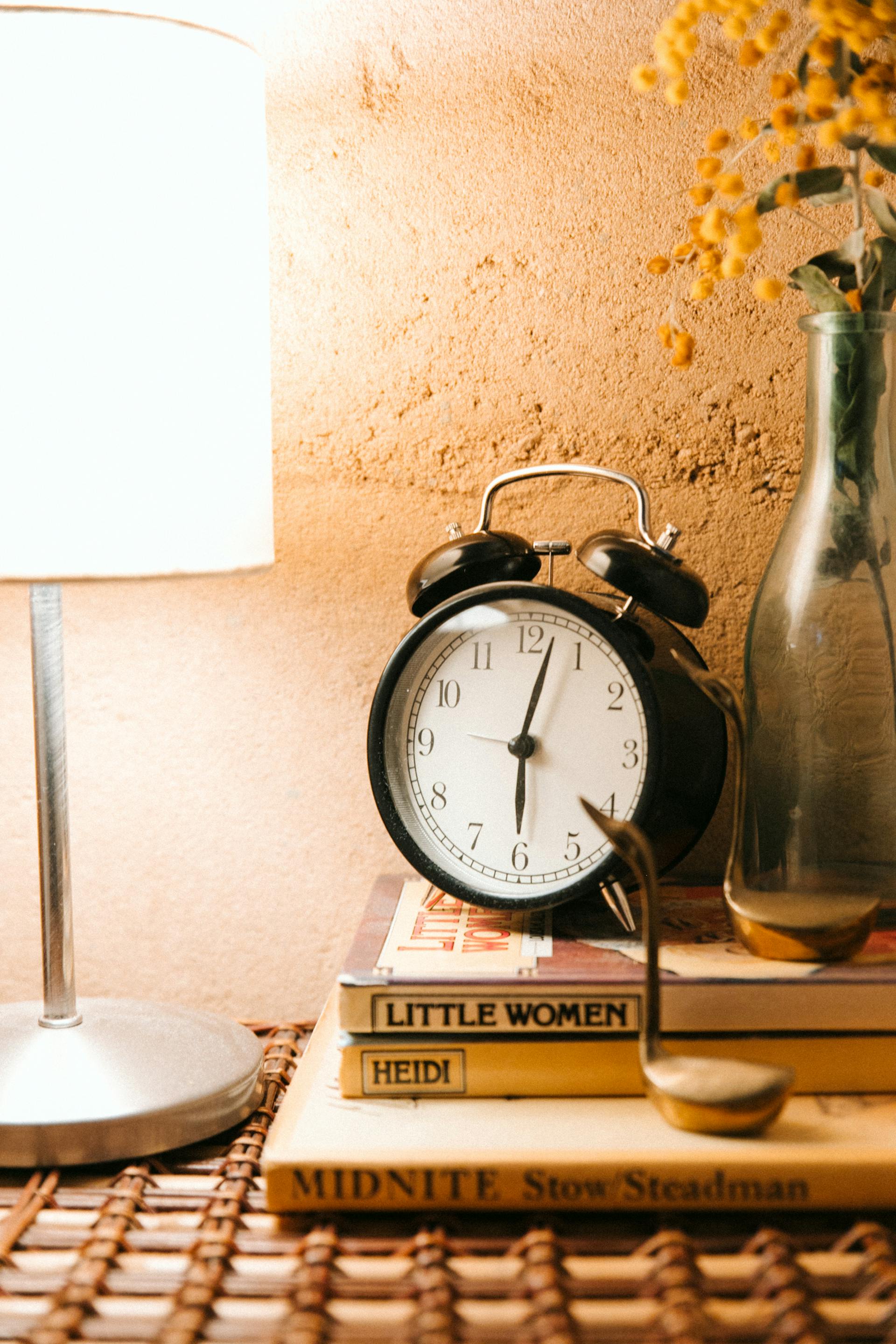 Un réveil vintage et une lampe lumineuse placés sur une table de chevet | Source : Pexels