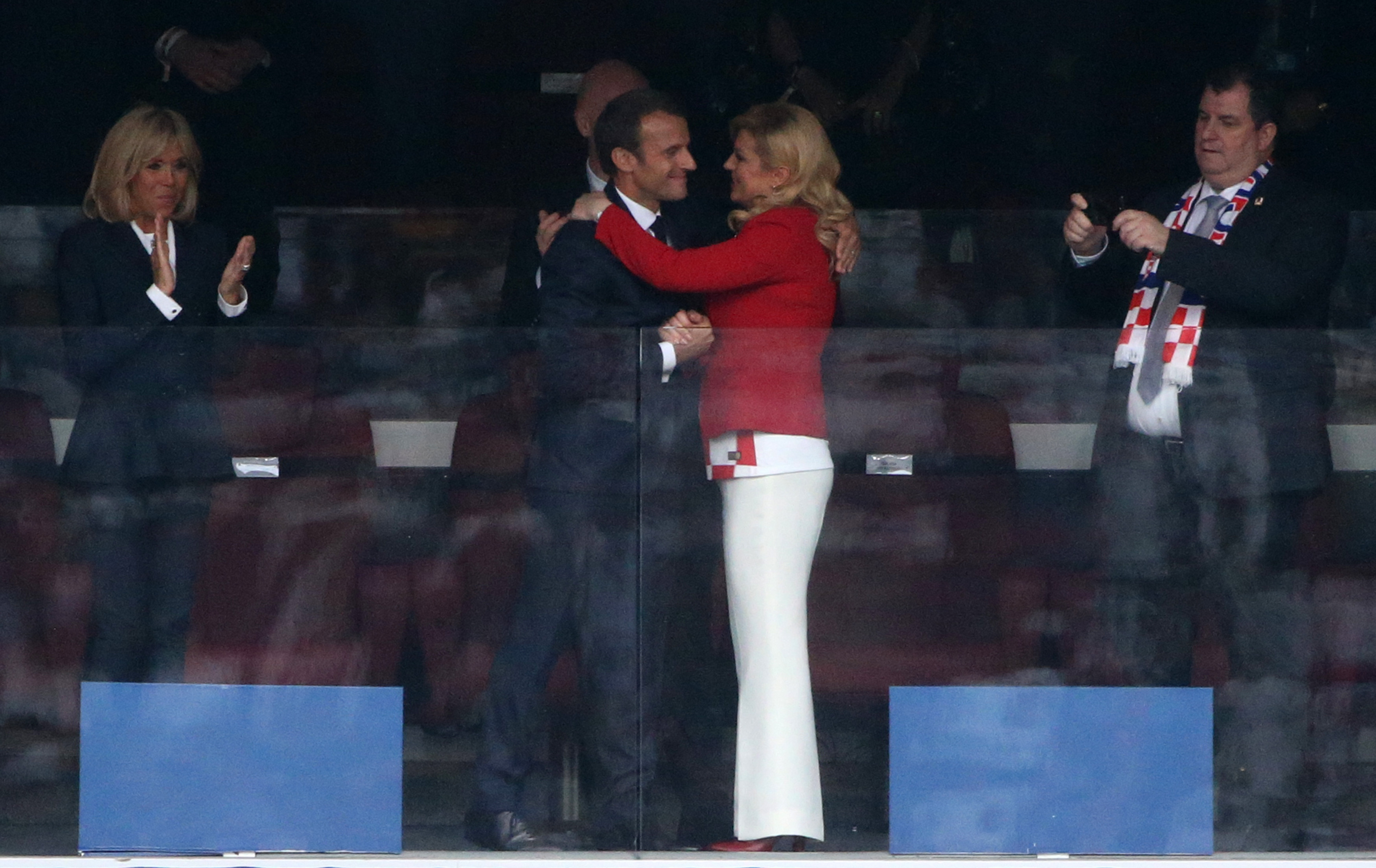 À un autre moment, Emmanuel Macron entoure Kolinda Grabar-Kitarović de ses deux bras dans une étreinte, tandis que Brigitte Macron se tient à proximité en applaudissant, observant la scène.