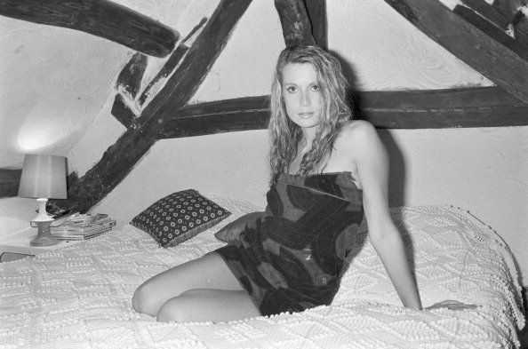 Catherine ALRIC, les cheveux mouillés, enveloppée d'une serviette éponge, assise sur son lit dans une chambre mansardée. | Photo : Getty Images