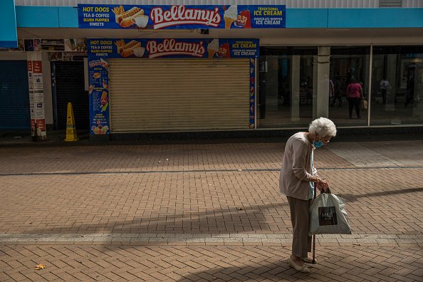 Un piéton âgé portant un masque facial passe devant une rangée de magasins fermés |Photo : Getty Images