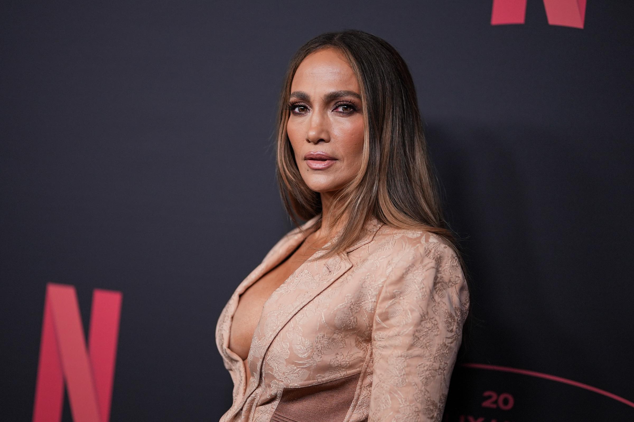 Jennifer Lopez se tient à l'angle de la caméra dans une robe de couleur blush avec des détails de corset structuré, des panneaux de satin et un décolleté plongeant. Ses cheveux lisses, son maquillage doux et neutre et son expression posée ajoutent de l'élégance à l'apparence de l'événement Netflix.