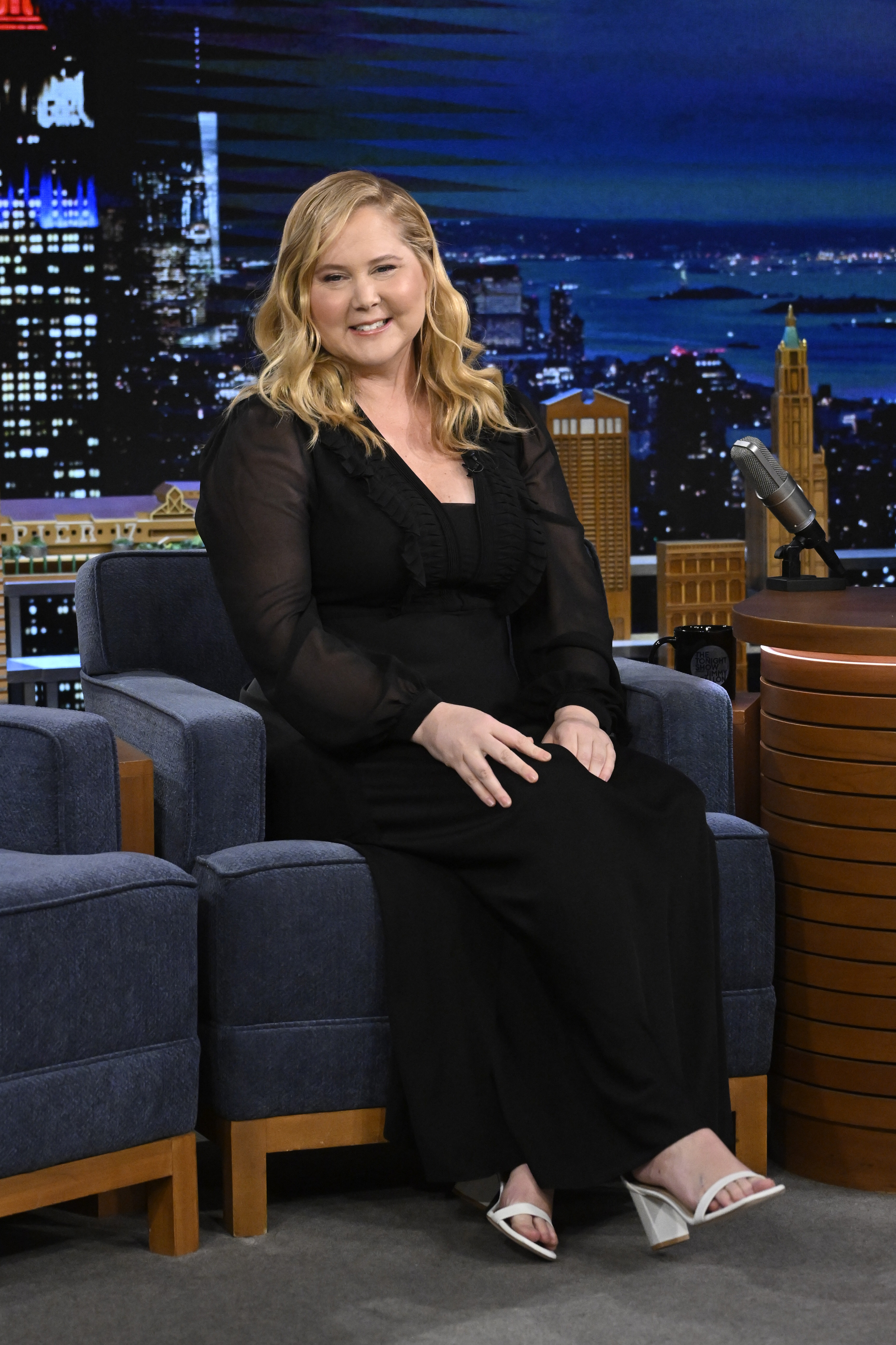 Amy Schumer dans l'émission « The Tonight Show Starring Jimmy Fallon » le 13 février 2024, vêtue d'une robe noire longue aux manches transparentes. Assise, le sourire détendu et les cheveux légèrement ondulés, elle rayonnait de confiance et de chaleur.