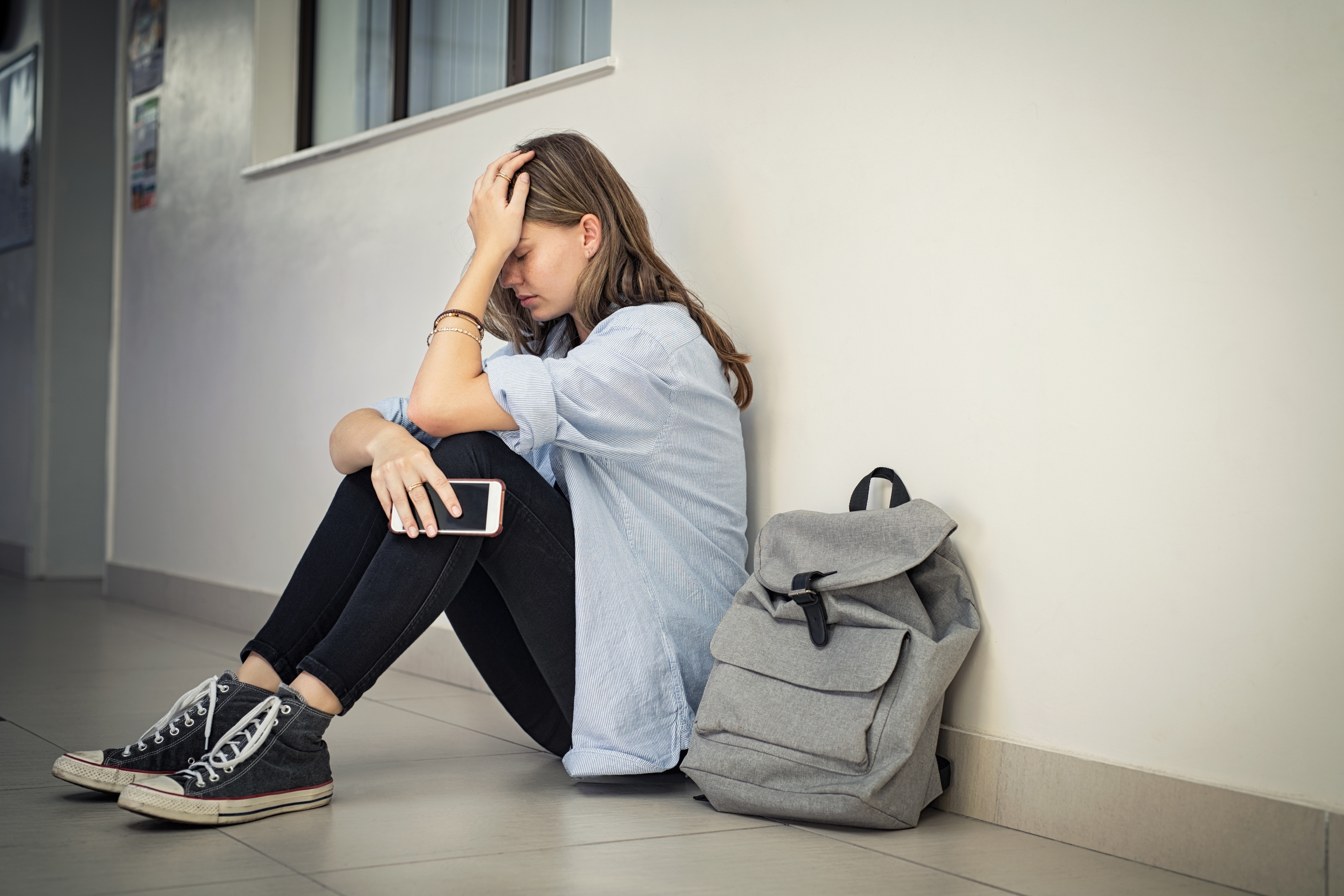 Une femme bouleversée et déprimée tient son smartphone sur le sol du campus universitaire tout en se tenant la tête | Source : Getty Images