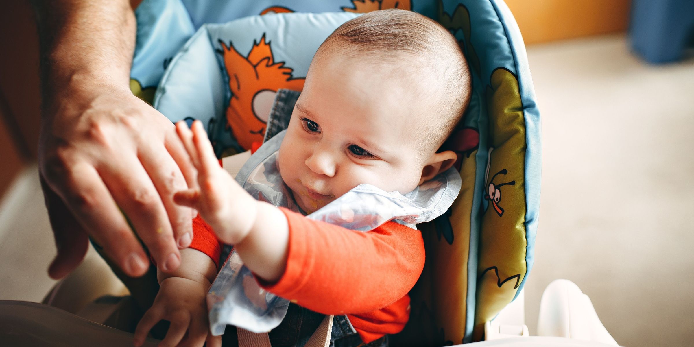 Gros plan sur un bébé dans sa chaise haute qui tend les bras vers ses parents | Source : Pexels