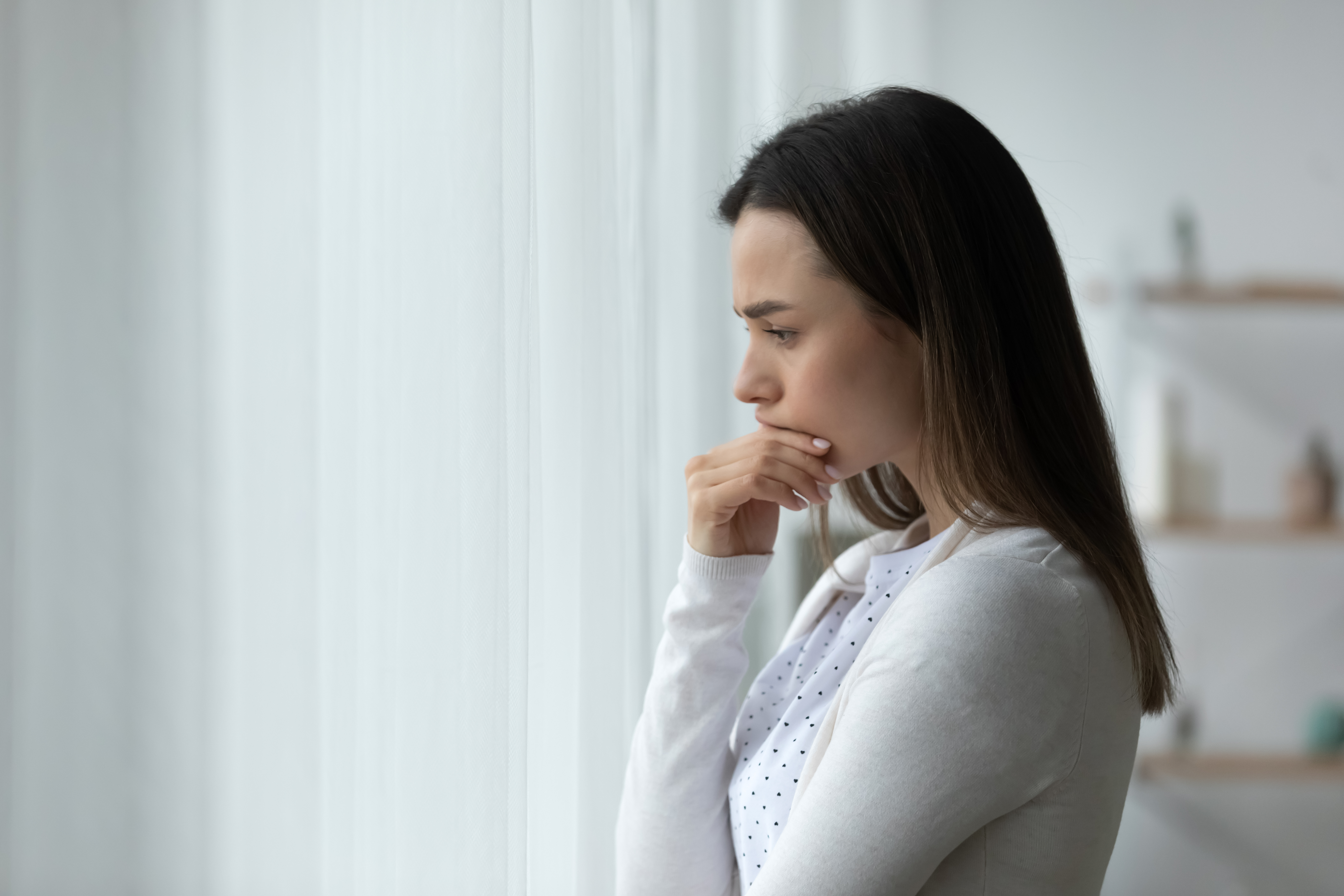 Mujer de pie en una habitación reflexionando sobre sus problemas. | Fuente: Shutterstock