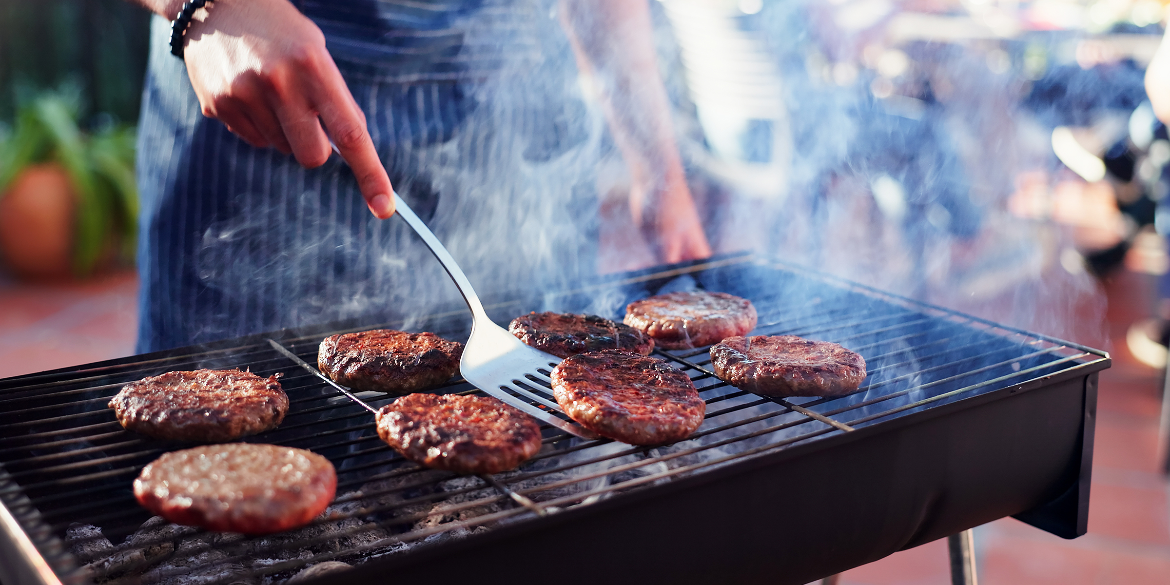 Une personne faisant griller des hamburgers sur un barbecue fumant dans l'arrière-cour | Source : Shutterstock