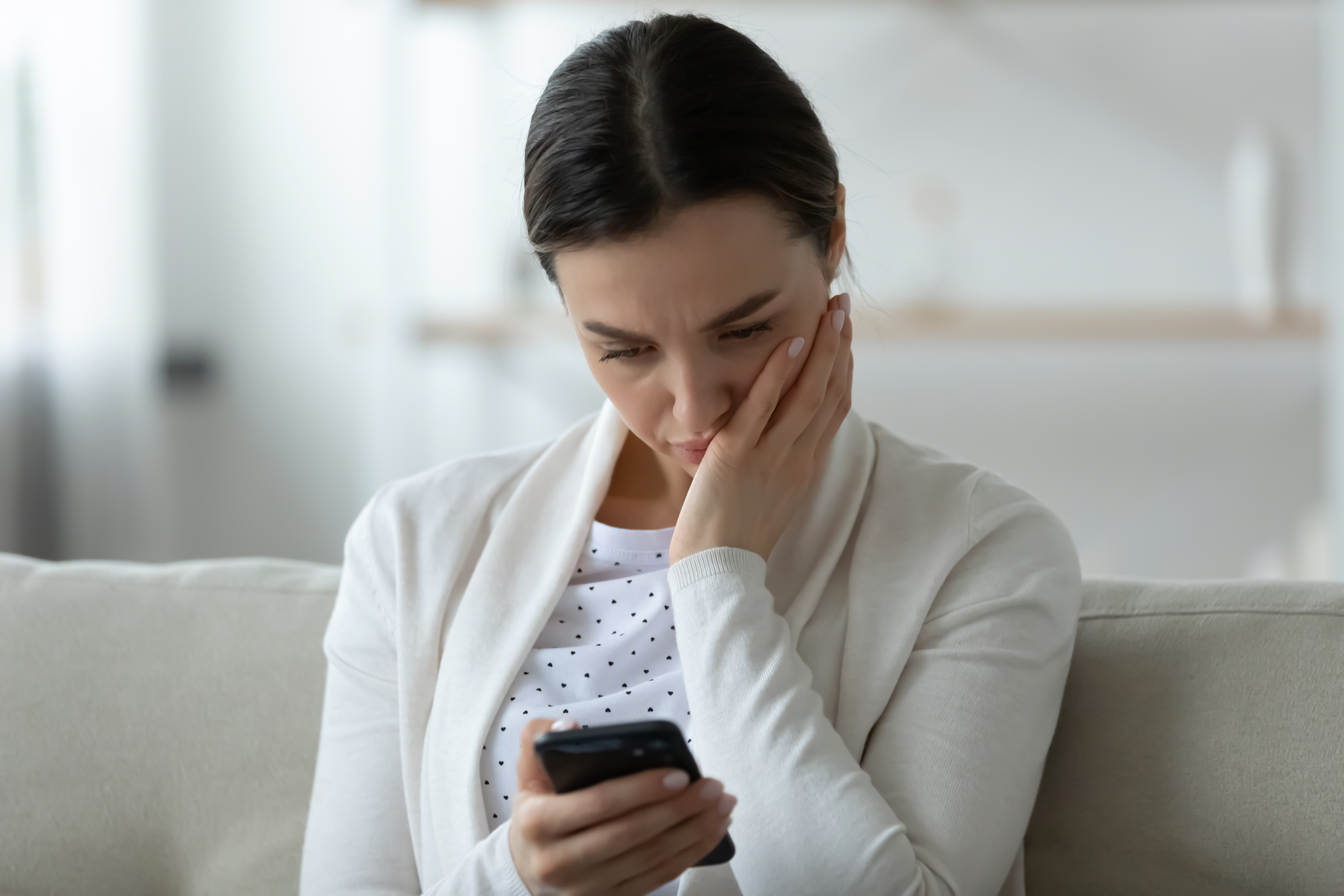 Une femme désemparée qui tient et regarde son smartphone | Source : Shutterstock