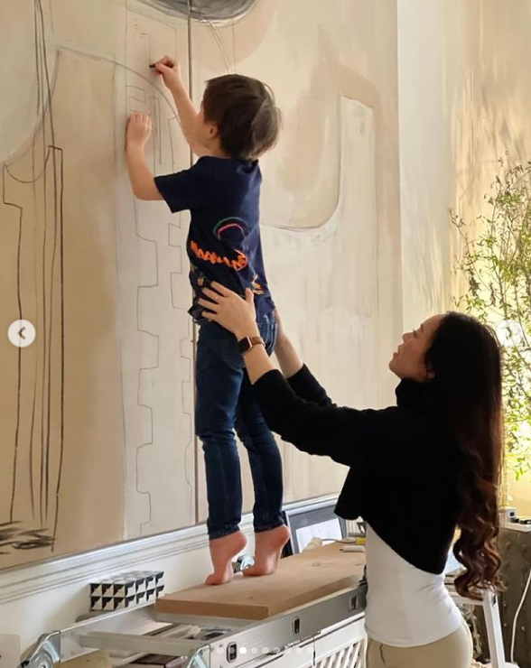 Christopher Woolf Mapelli Mozzi montre ses talents artistiques en dessinant sur un portrait pendant que sa mère, Dara Huang, le tient par derrière. | Source : Instagram/dara_huang