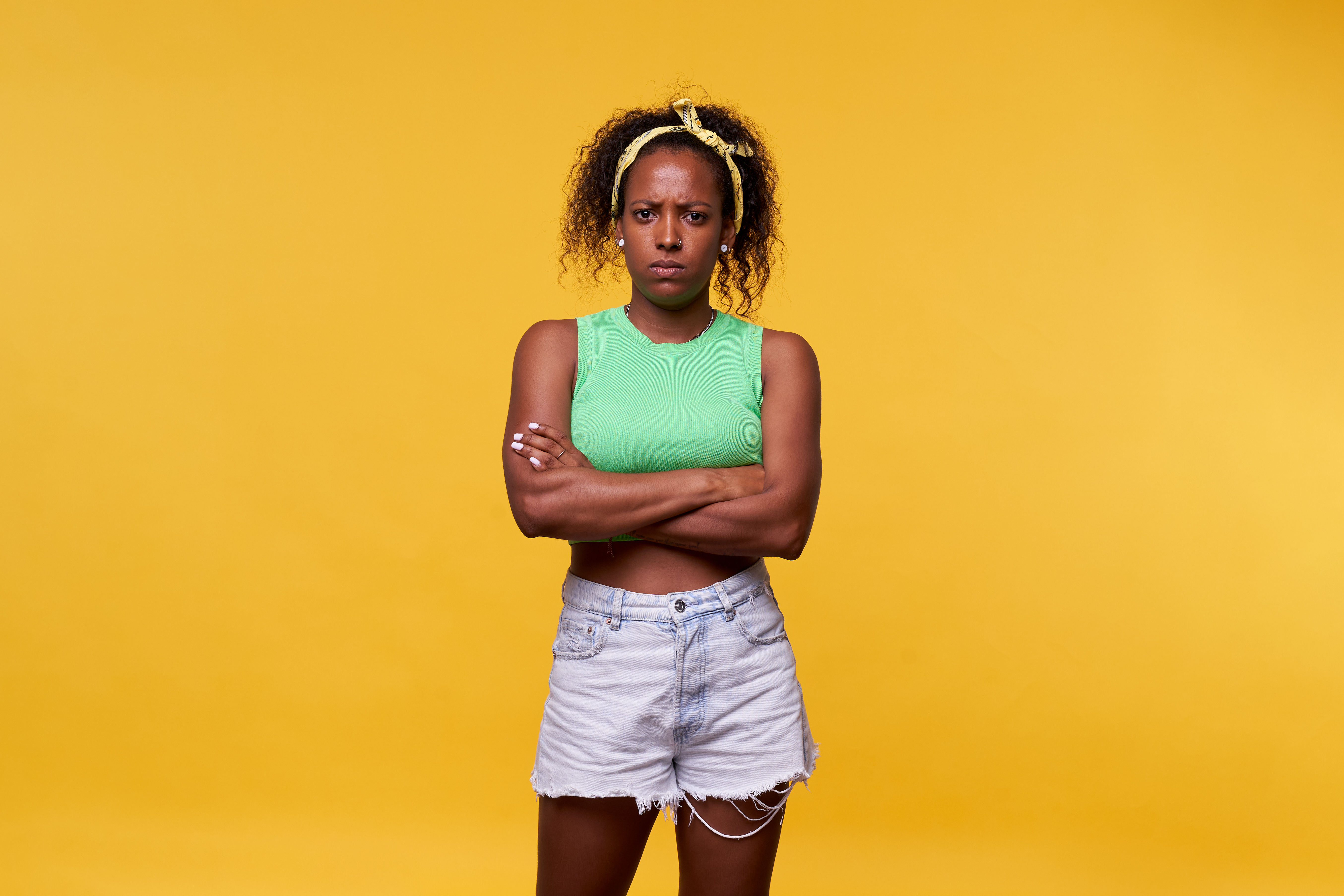 Photo d'une femme latine en colère, debout sur un fond jaune, croisant les bras et regardant l'appareil photo avec sérieux. Image isolée dans un studio | Source : Getty Images