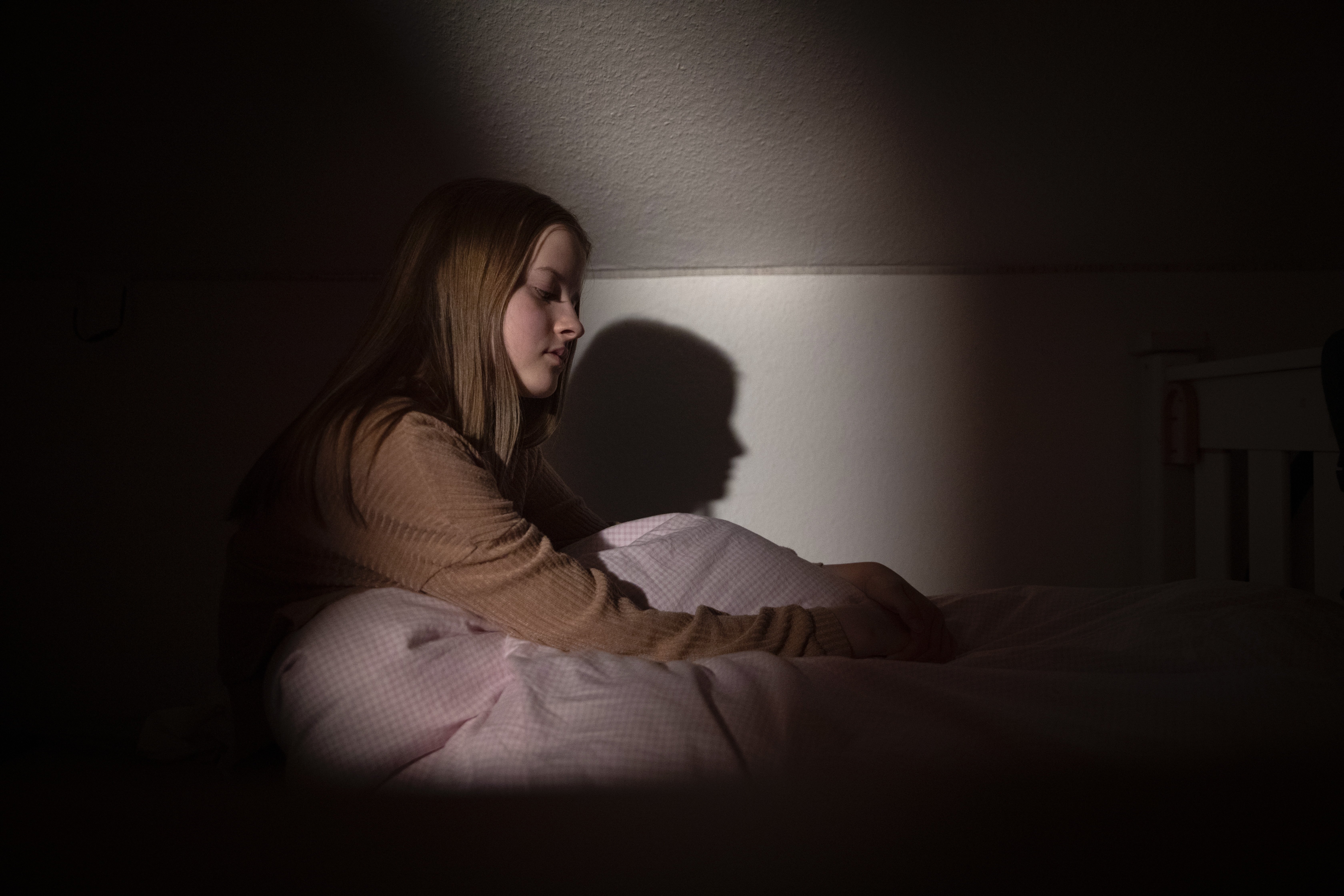 Adolescente assise dans son lit, la nuit, dans une lumière faible, avec une expression faciale décrivant le désespoir et la tristesse | Source : Getty Images