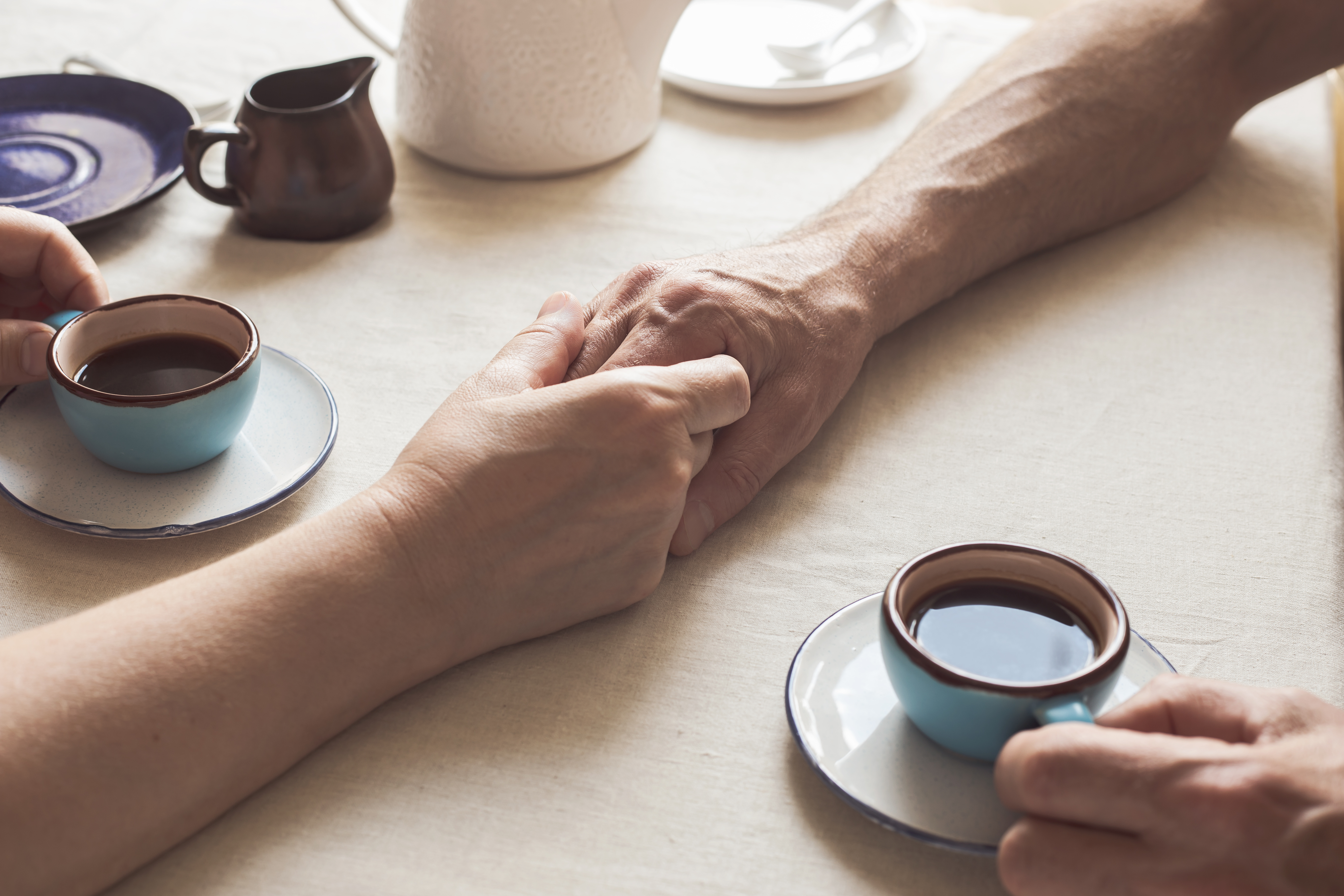 Image recadrée d'un couple de seniors se tenant par la main et buvant un café | Source : Getty Images