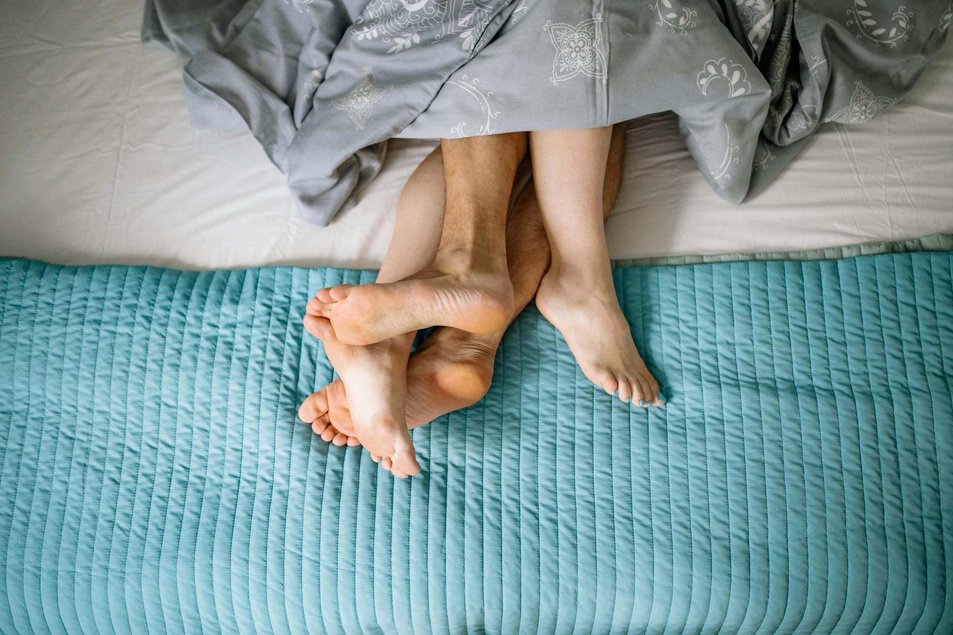 Gros plan sur les jambes d'un couple entrelacées dans le lit | Source : Pexels