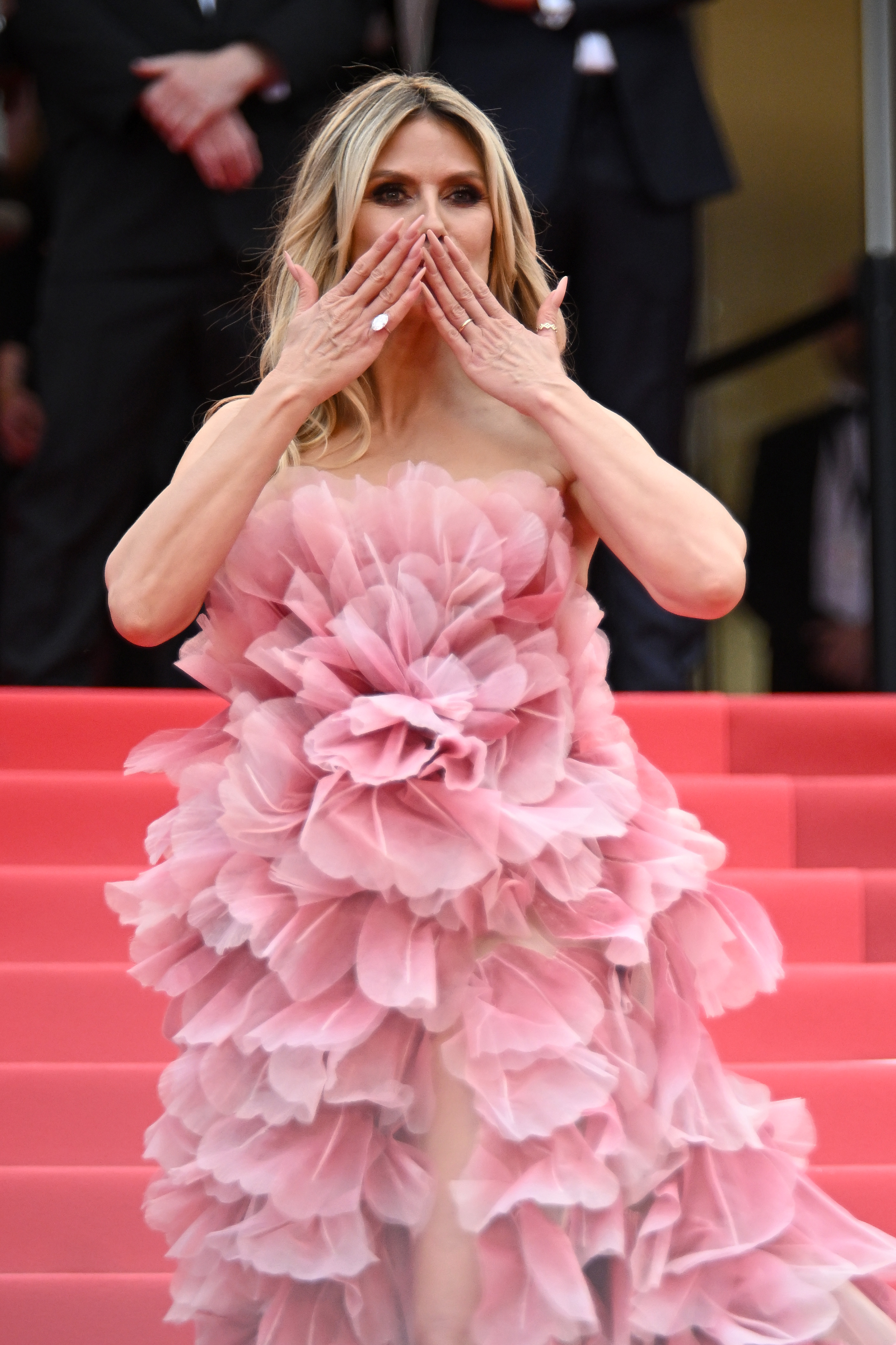 Même après avoir contourné les règles, Heidi Klum rayonne de joie sur le tapis rouge - capturée en plein milieu d'un baiser ludique, elle exhibe ses ongles manucurés et ses bagues scintillantes, se délectant manifestement de ce moment.