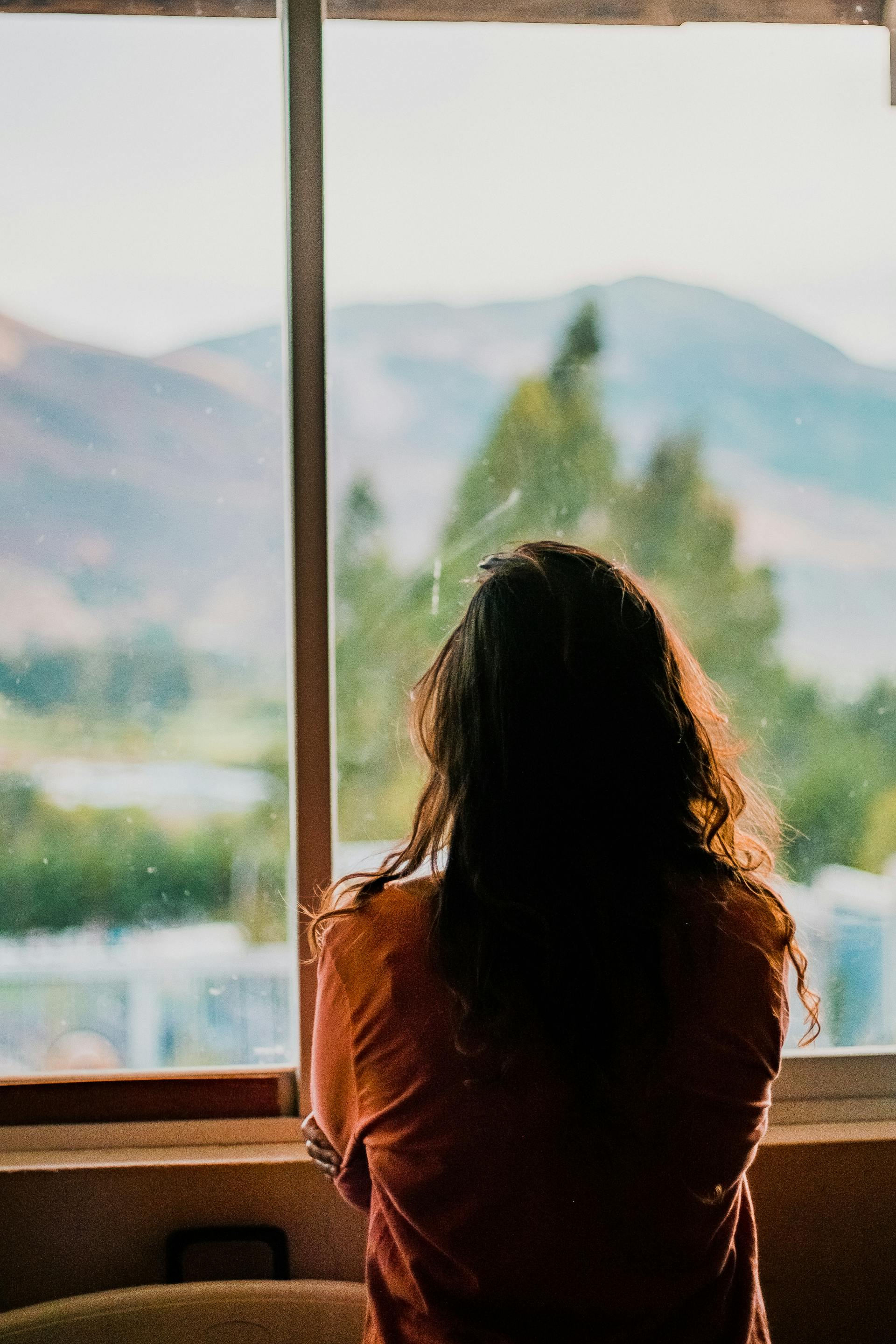 Plan arrière d'une femme regardant par la fenêtre avec les bras croisés | Source : Pexels