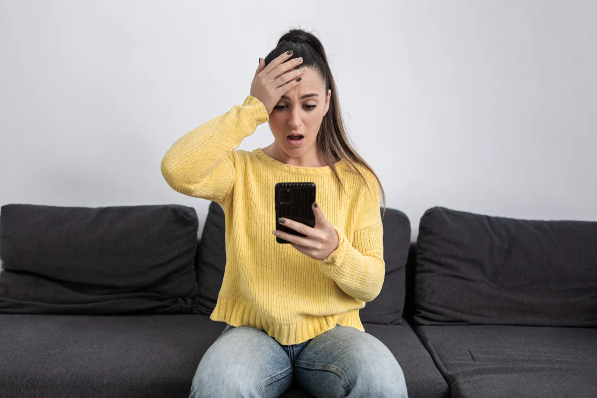 Une femme est choquée alors qu'elle regarde l'écran de son téléphone portable | Source : Getty Images