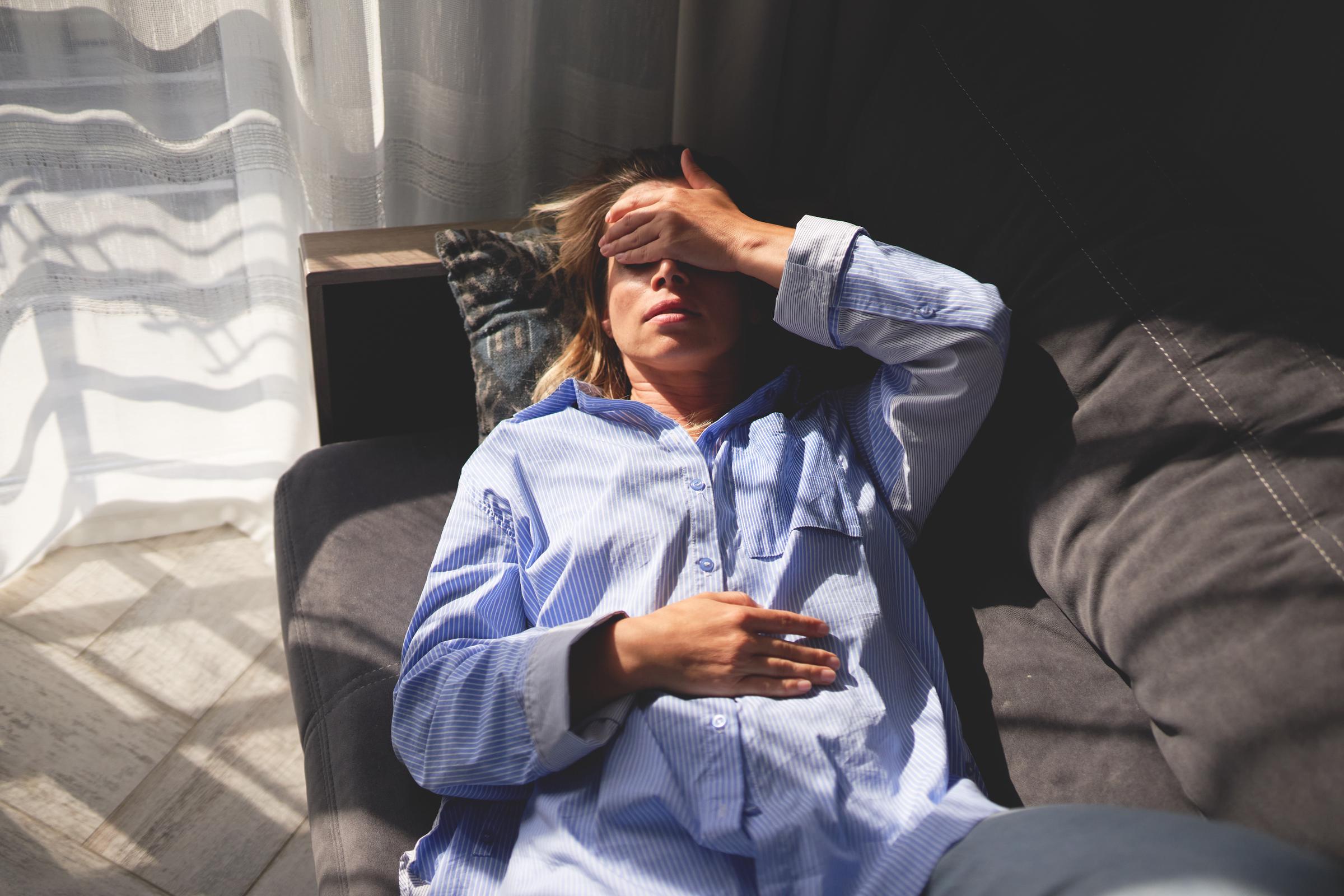Femme allongée sur un canapé, la main sur le front et les yeux fermés, indiquant l'épuisement ou le stress | Source : Getty Images