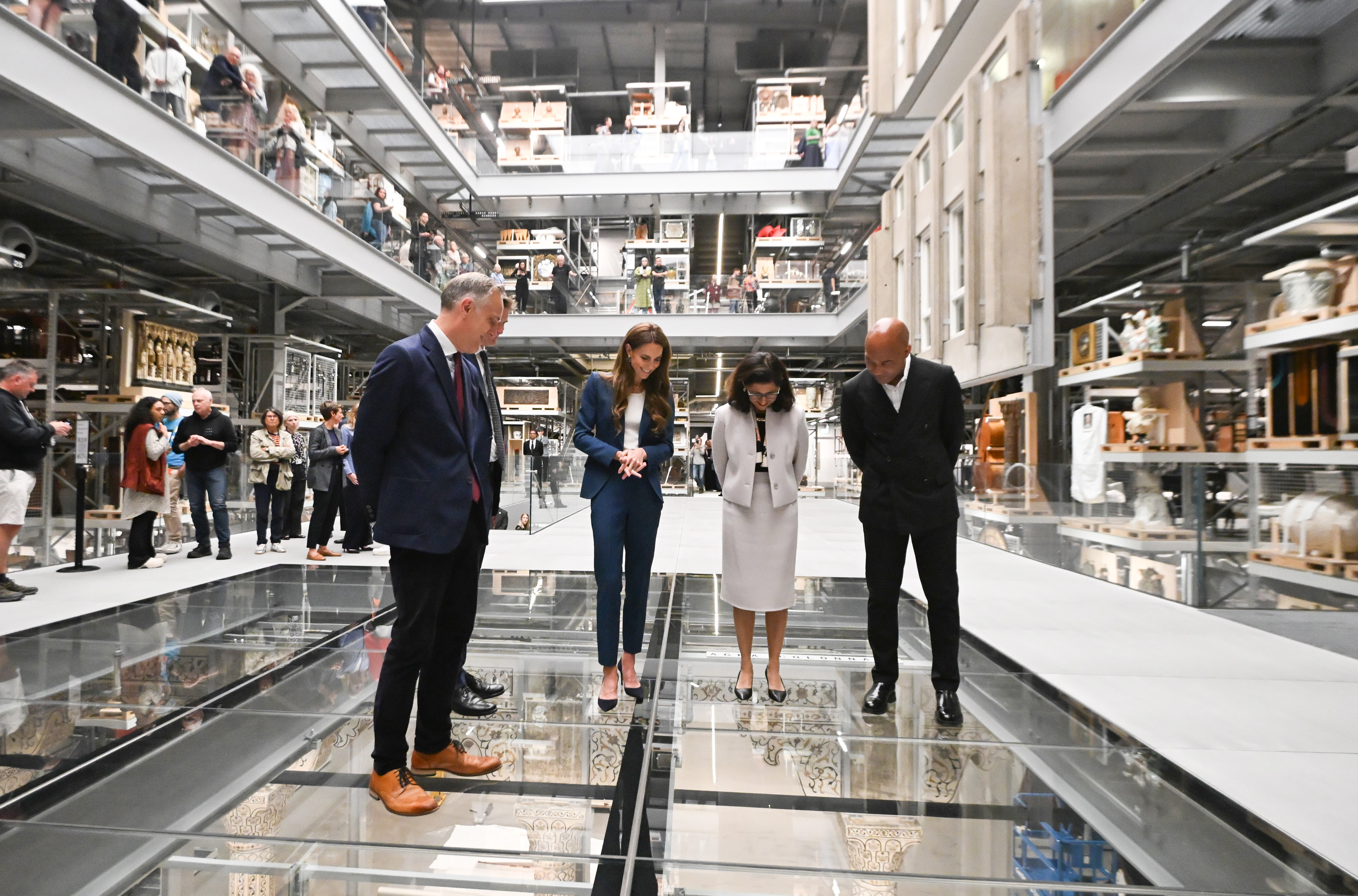 Debout au-dessus d'un plancher de verre, la princesse Catherine observe l'exposition en contrebas avec d'autres responsables du musée. Son regard est dirigé vers le bas, sa posture prudente, suggérant à la fois la curiosité et la prudence alors qu'elles explorent l'espace d'exposition vertical.
